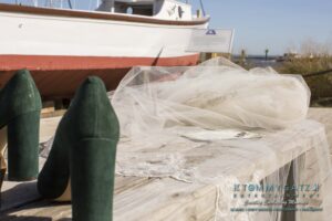 Green high heels and a veil on a wooden table, with a boat in the background.