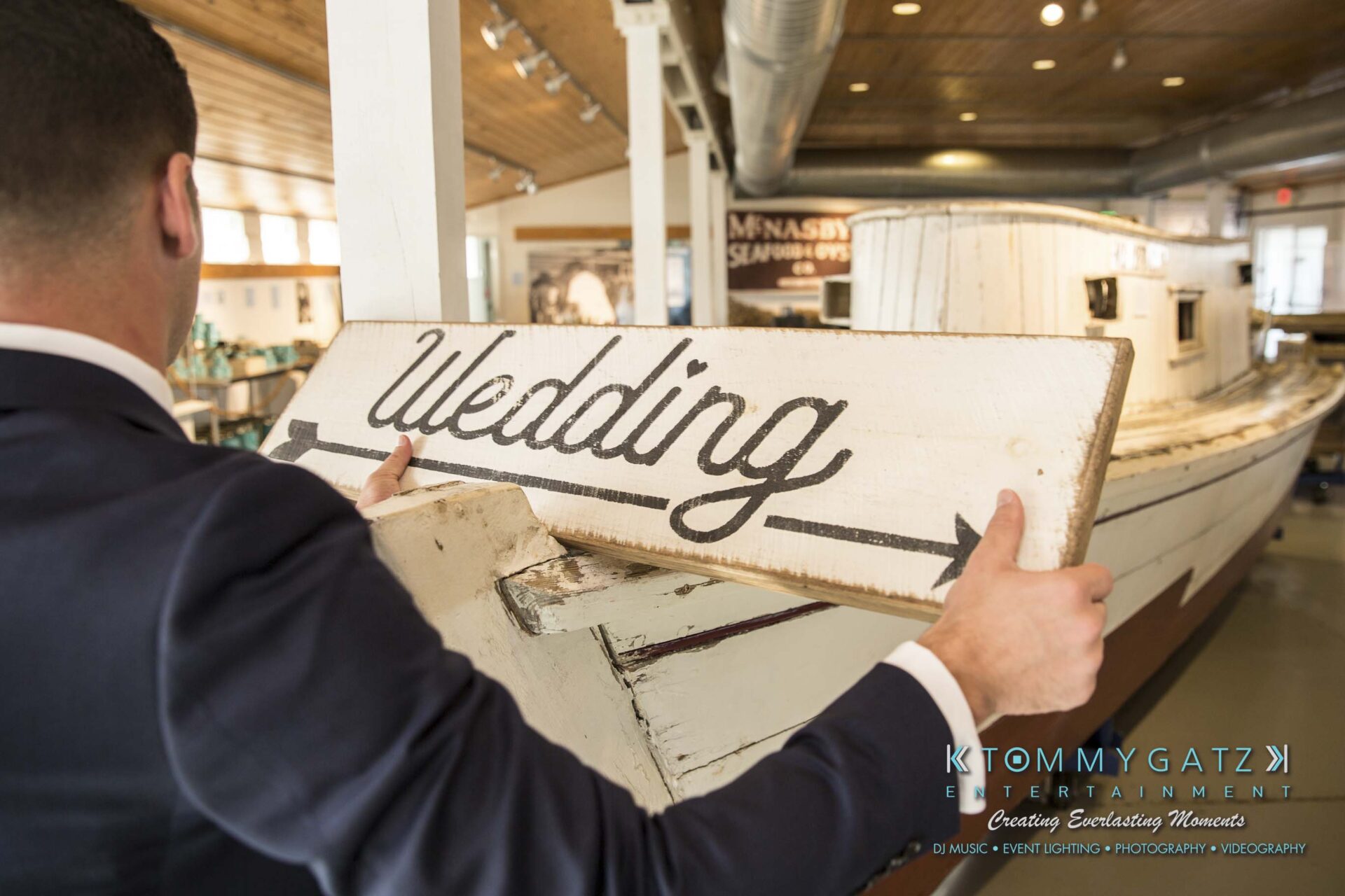 Person holding a wooden "Wedding" sign in a room with a boat and various decorations.
