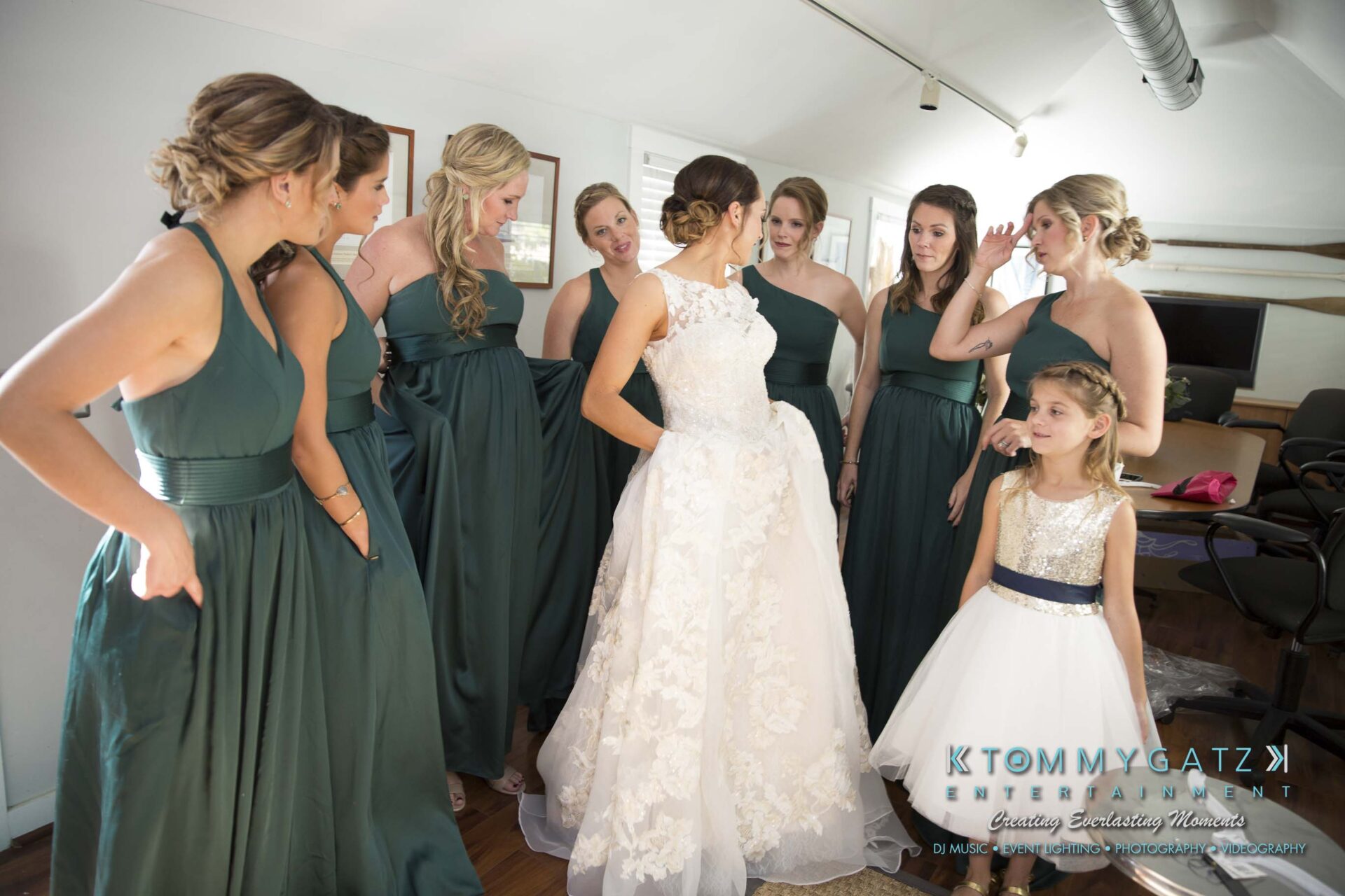 Amanda-Tyler-102117-PREP-Low-Res-WM-42 - TOMMY GATZ ENTERTAINMENT A bride in a white dress is surrounded by bridesmaids in green dresses and a young girl in a white dress standing indoors.