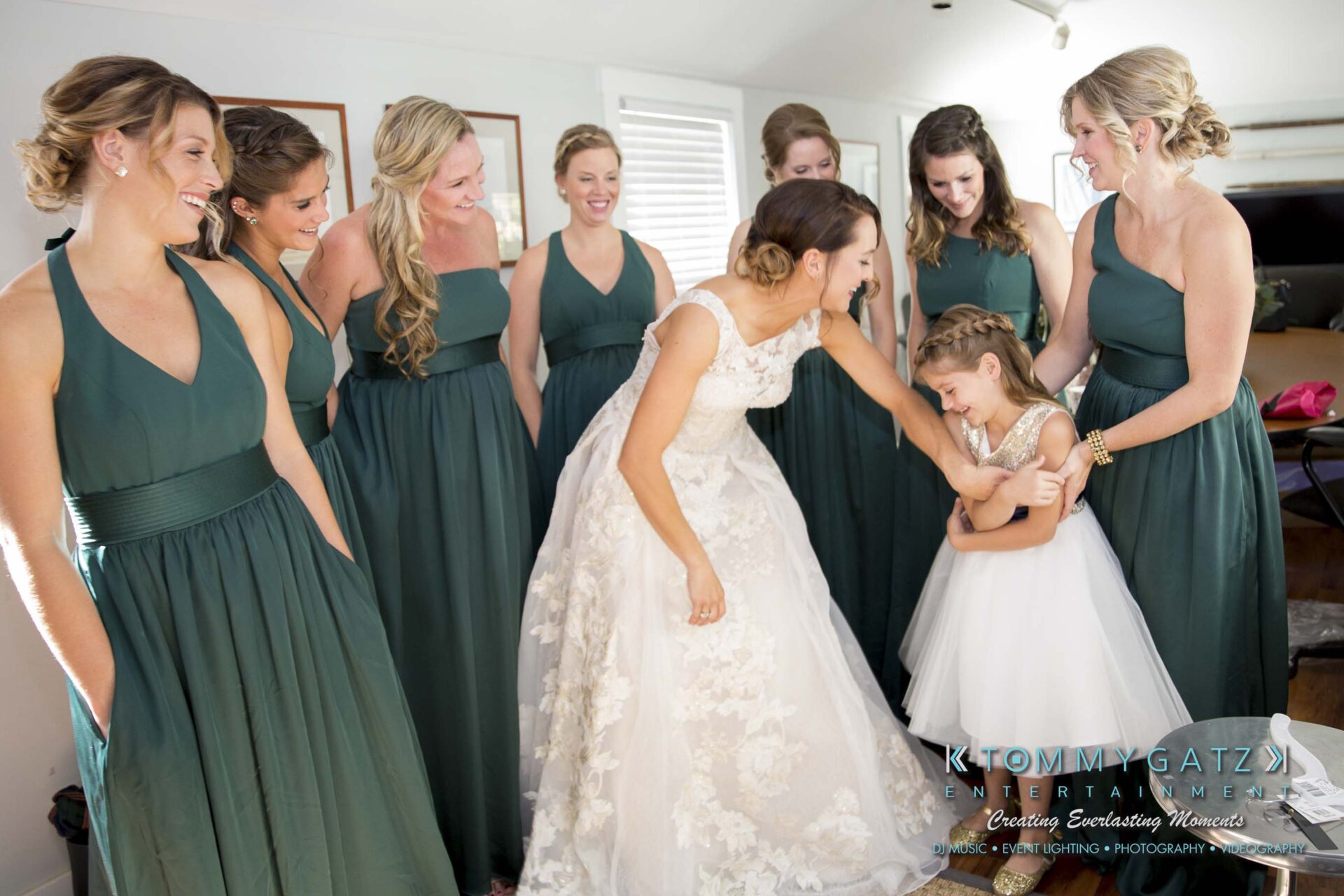 Amanda-Tyler-102117-PREP-Low-Res-WM-50 - TOMMY GATZ ENTERTAINMENT A bride in a white gown interacts joyfully with a young girl in a white dress, surrounded by bridesmaids in green dresses.