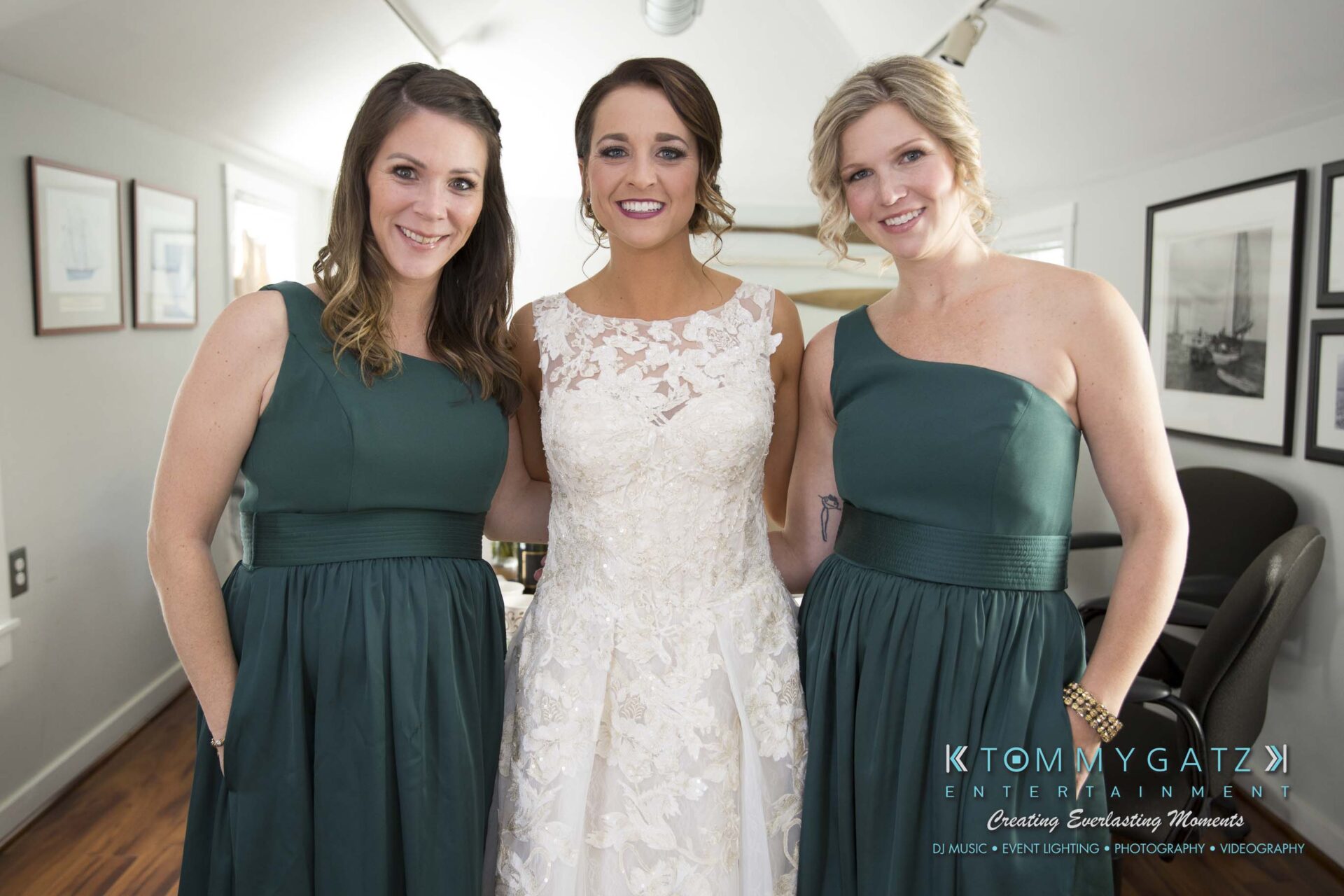 Amanda-Tyler-102117-PREP-Low-Res-WM-52 - TOMMY GATZ ENTERTAINMENT Three women indoors, with two wearing green dresses and one in a white bridal gown, smiling at the camera.