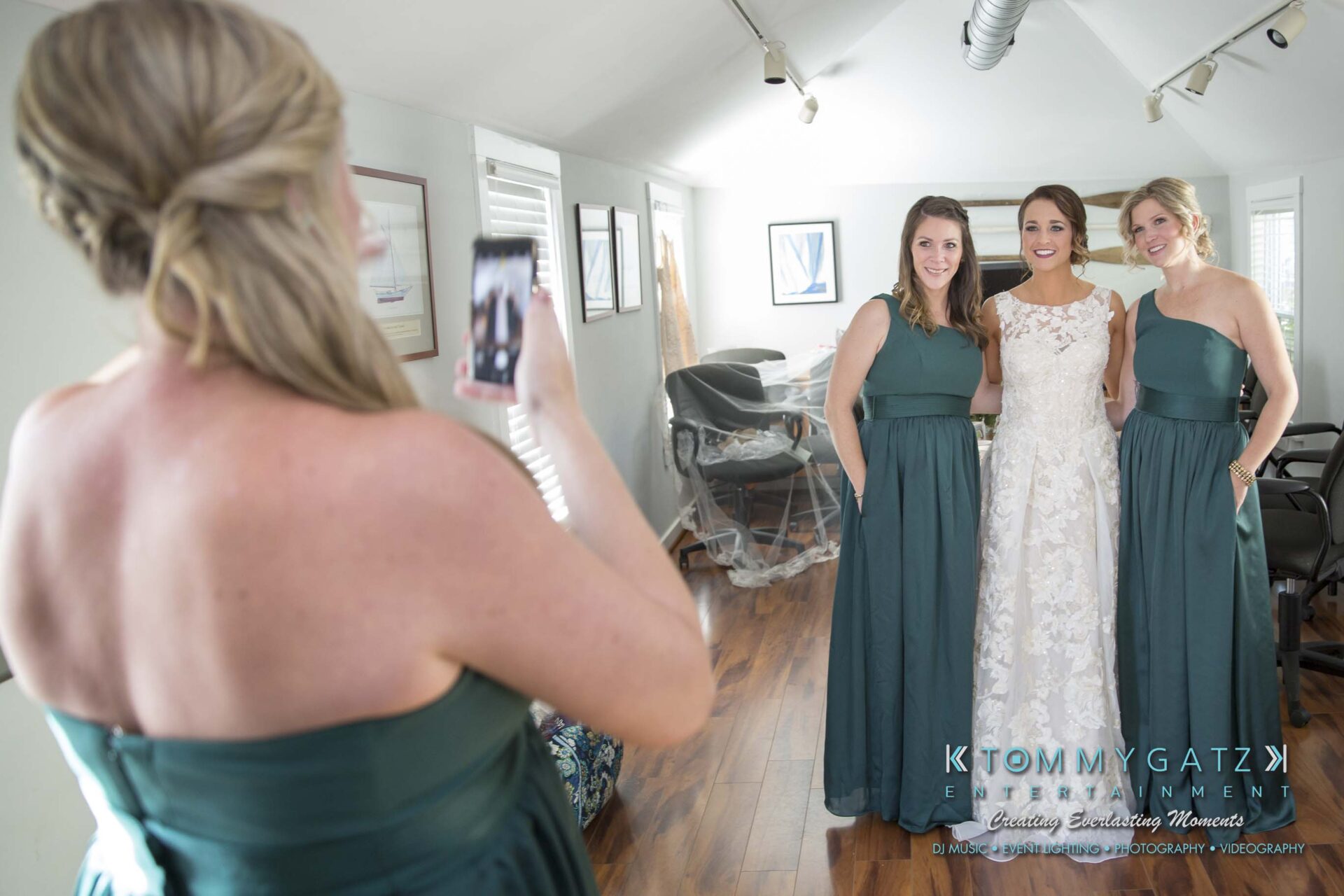 Amanda-Tyler-102117-PREP-Low-Res-WM-53 - TOMMY GATZ ENTERTAINMENT A bride in a white dress poses with two bridesmaids in green dresses while another person takes a photo in a well-lit room.