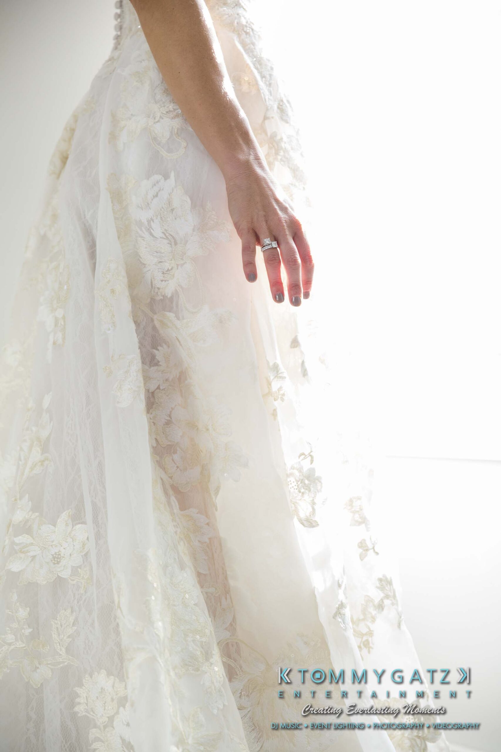 Amanda-Tyler-102117-PREP-Low-Res-WM-57 - TOMMY GATZ ENTERTAINMENT A close-up of a bride's hand with a ring, resting against the lace fabric of a wedding dress.
