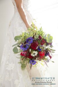 Amanda-Tyler-102117-PREP-Low-Res-WM-60 - TOMMY GATZ ENTERTAINMENT Bride in a lace gown holds a bouquet of red and purple flowers with greenery.