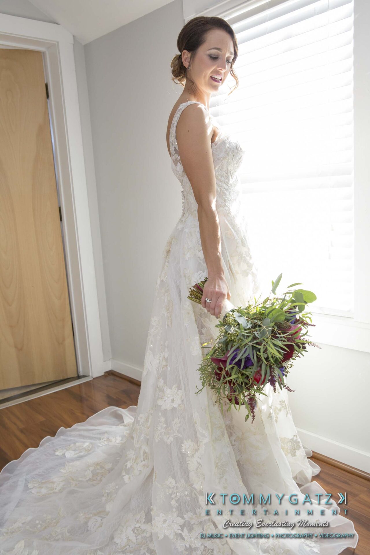 Amanda-Tyler-102117-PREP-Low-Res-WM-63 - TOMMY GATZ ENTERTAINMENT A bride in a white lace dress holds a bouquet, standing by a window.
