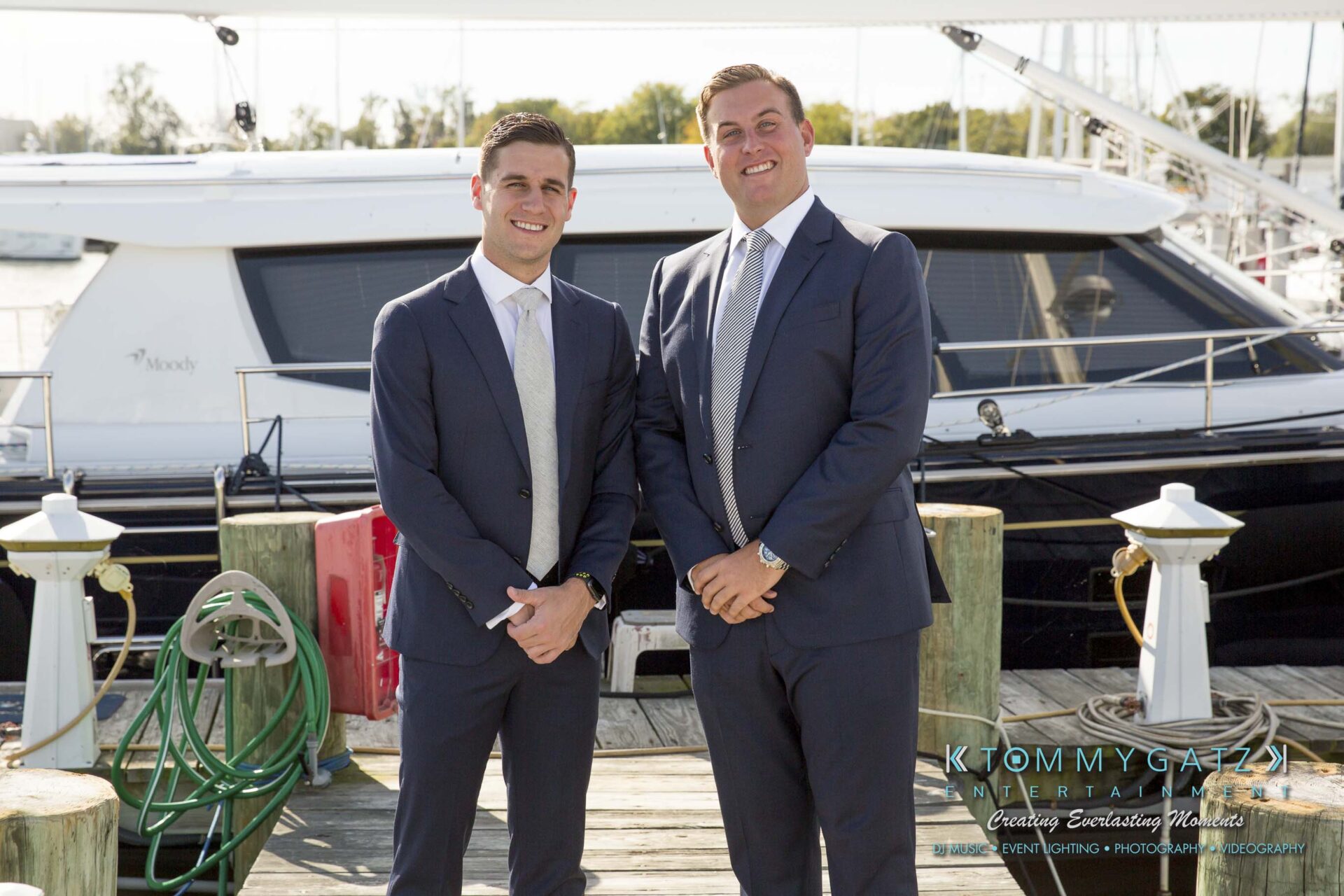Amanda-Tyler-102117-PREP-Low-Res-WM-87 - TOMMY GATZ ENTERTAINMENT Two people in suits stand on a dock in front of a yacht, smiling at the camera.