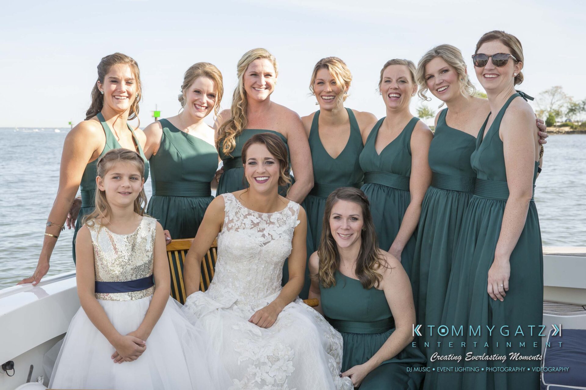 Amanda-Tyler-102117-PREP-Low-Res-WM-96 - TOMMY GATZ ENTERTAINMENT A bride in a white dress poses with nine women in green dresses on a boat by the water.