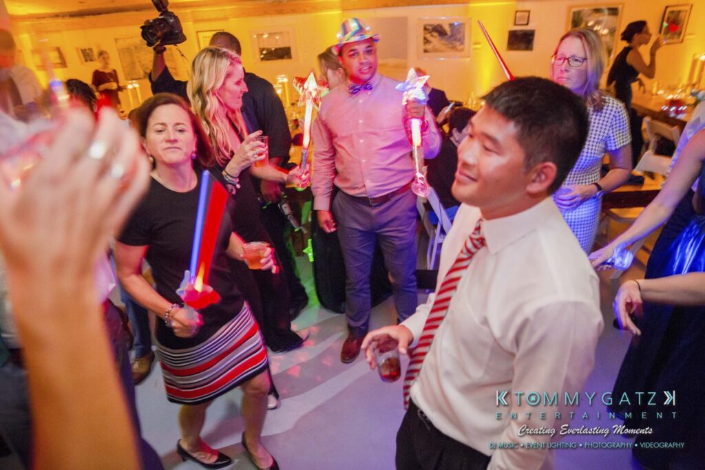 People dancing and holding light sticks at a party, with colorful lighting and festive attire.