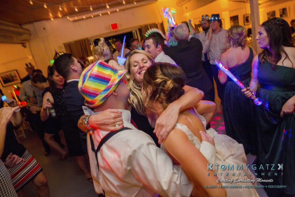 People are dancing and hugging at a lively indoor party with colorful lights and festive attire.