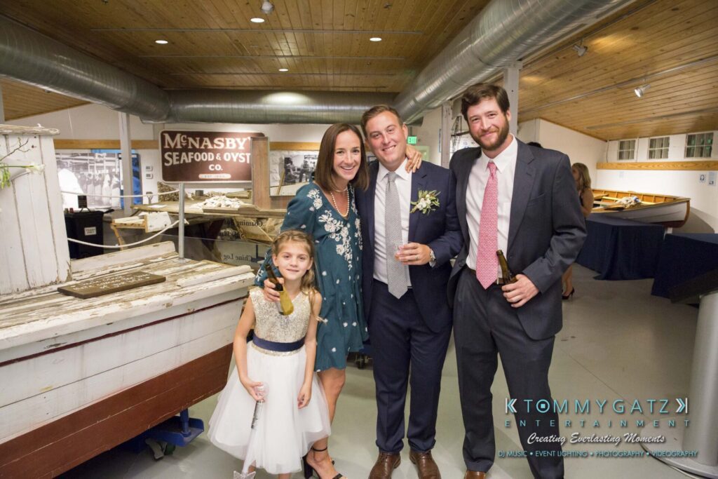 Amanda-Tyler-102117-RECEPTION-Low-Res-WM-187 - TOMMY GATZ ENTERTAINMENT A group of four people, elegantly dressed, stand inside a maritime-themed venue. A young girl in a dress stands next to a woman, along with two men in suits. .