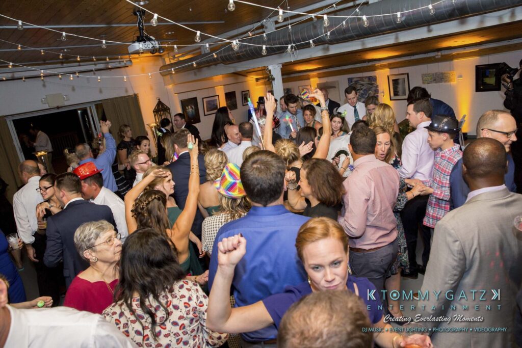 A lively party scene with people dancing and mingling in a decorated venue. Some are wearing party hats.