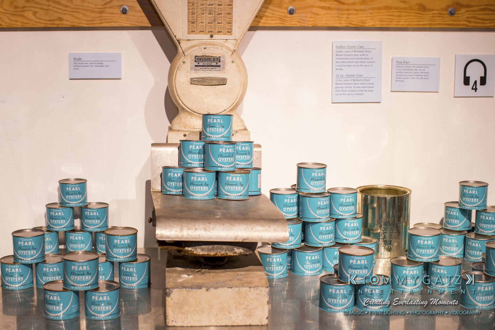 Amanda-Tyler-102117-RECEPTION-Low-Res-WM-20 - TOMMY GATZ ENTERTAINMENT An old weighing scale surrounded by stacked cans of Pearl Brand oysters with turquoise labels on display.
