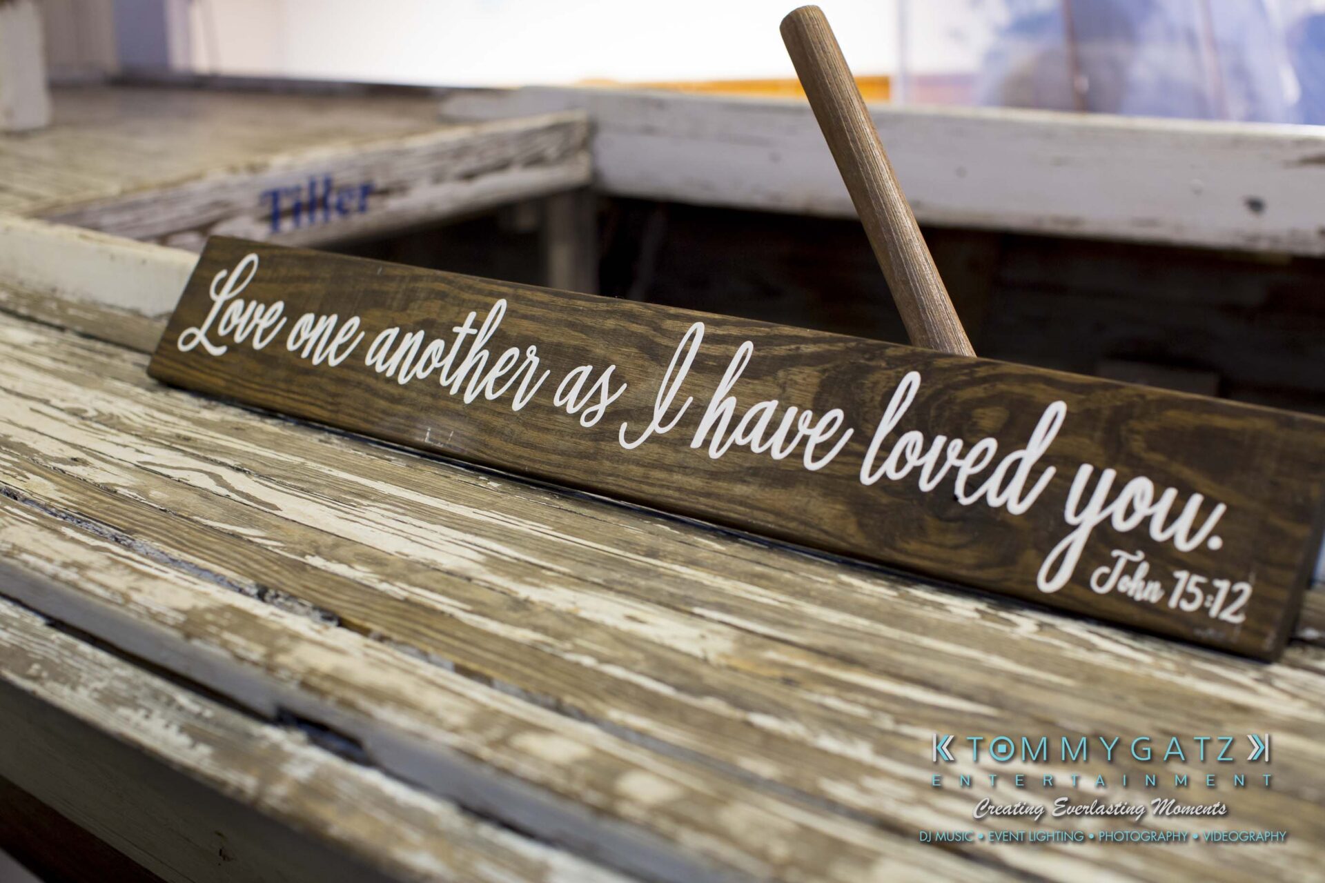 Amanda-Tyler-102117-RECEPTION-Low-Res-WM-21 - TOMMY GATZ ENTERTAINMENT A wooden sign with handwritten text: "Love one another as I have loved you. John 15:12" placed on a white wooden surface.