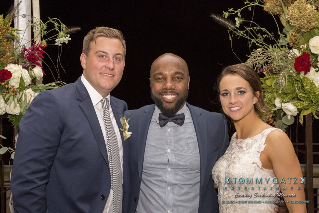 Three people posing together at an event, with flowers in the background.