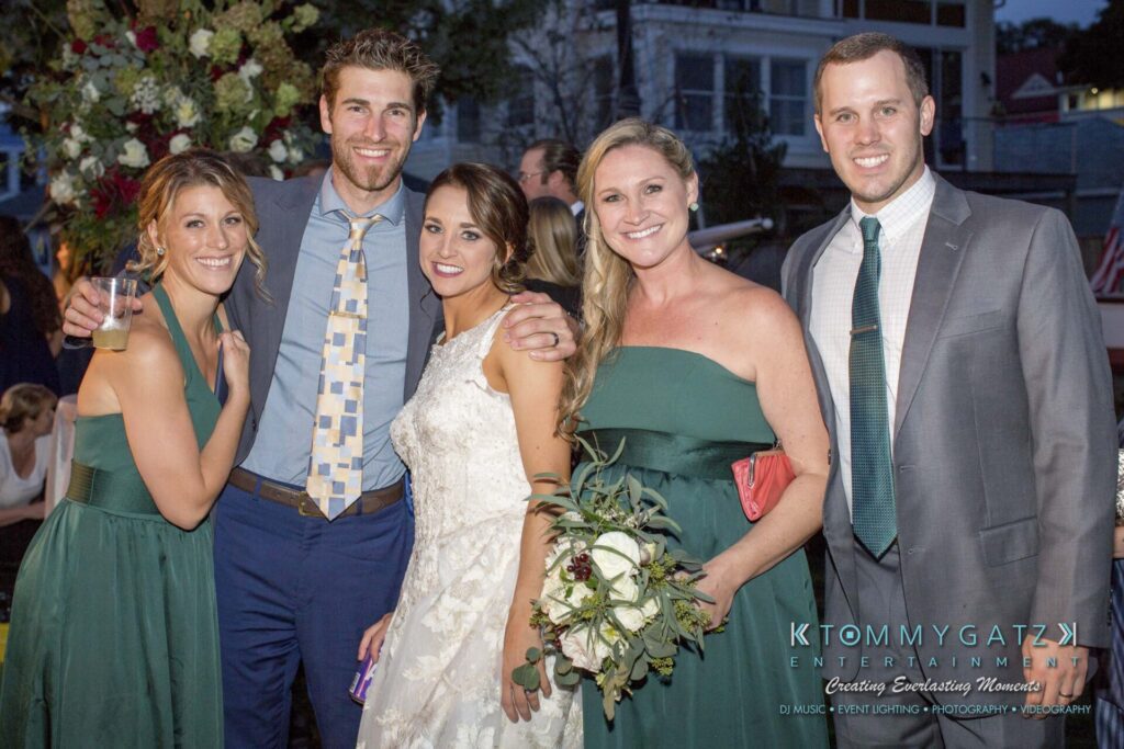Five people dressed in formal attire pose together outdoors at an event.