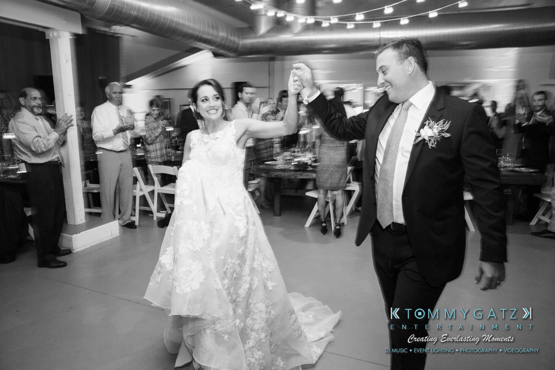 Amanda-Tyler-102117-RECEPTION-Low-Res-WM-39 - TOMMY GATZ ENTERTAINMENT A bride and groom dance joyfully in a venue adorned with guests applauding around them.