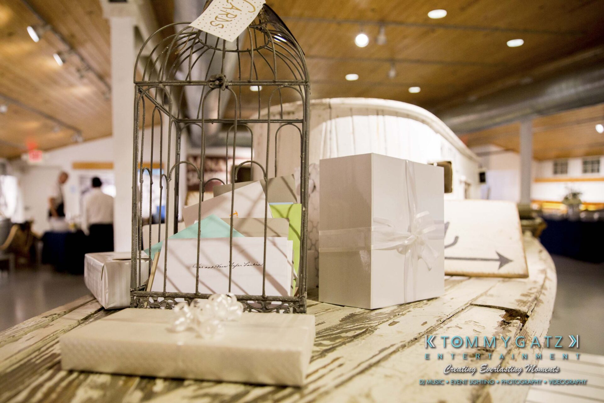Amanda-Tyler-102117-RECEPTION-Low-Res-WM-51 - TOMMY GATZ ENTERTAINMENT A decorative birdcage holds envelopes on a rustic table alongside wrapped gift boxes with bows in a warmly lit room.