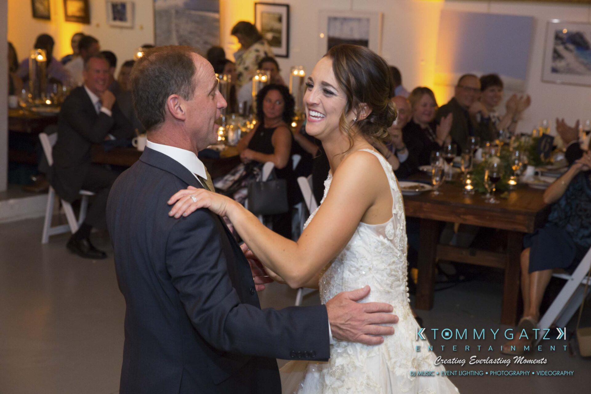 Amanda-Tyler-102117-RECEPTION-Low-Res-WM-73 - TOMMY GATZ ENTERTAINMENT Bride and groom smiling and dancing at a wedding reception, surrounded by seated guests.