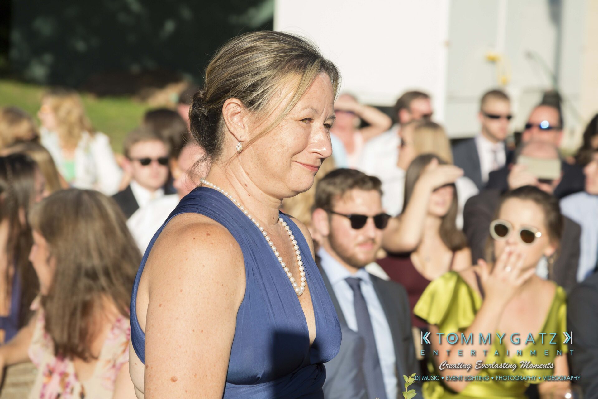 Ann-Marie-Alex-92317-CEREMONY-Low-Res-WM-23 - TOMMY GATZ ENTERTAINMENT A woman in a blue dress stands outdoors at an event, with people in the background.