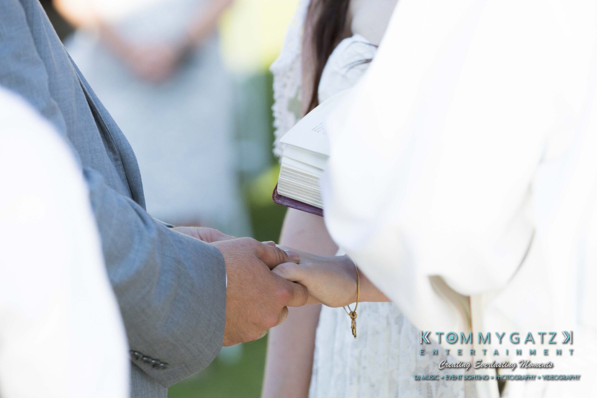Ann-Marie-Alex-92317-CEREMONY-Low-Res-WM-82 - TOMMY GATZ ENTERTAINMENT A couple holding hands during a wedding ceremony, with one person holding a book.