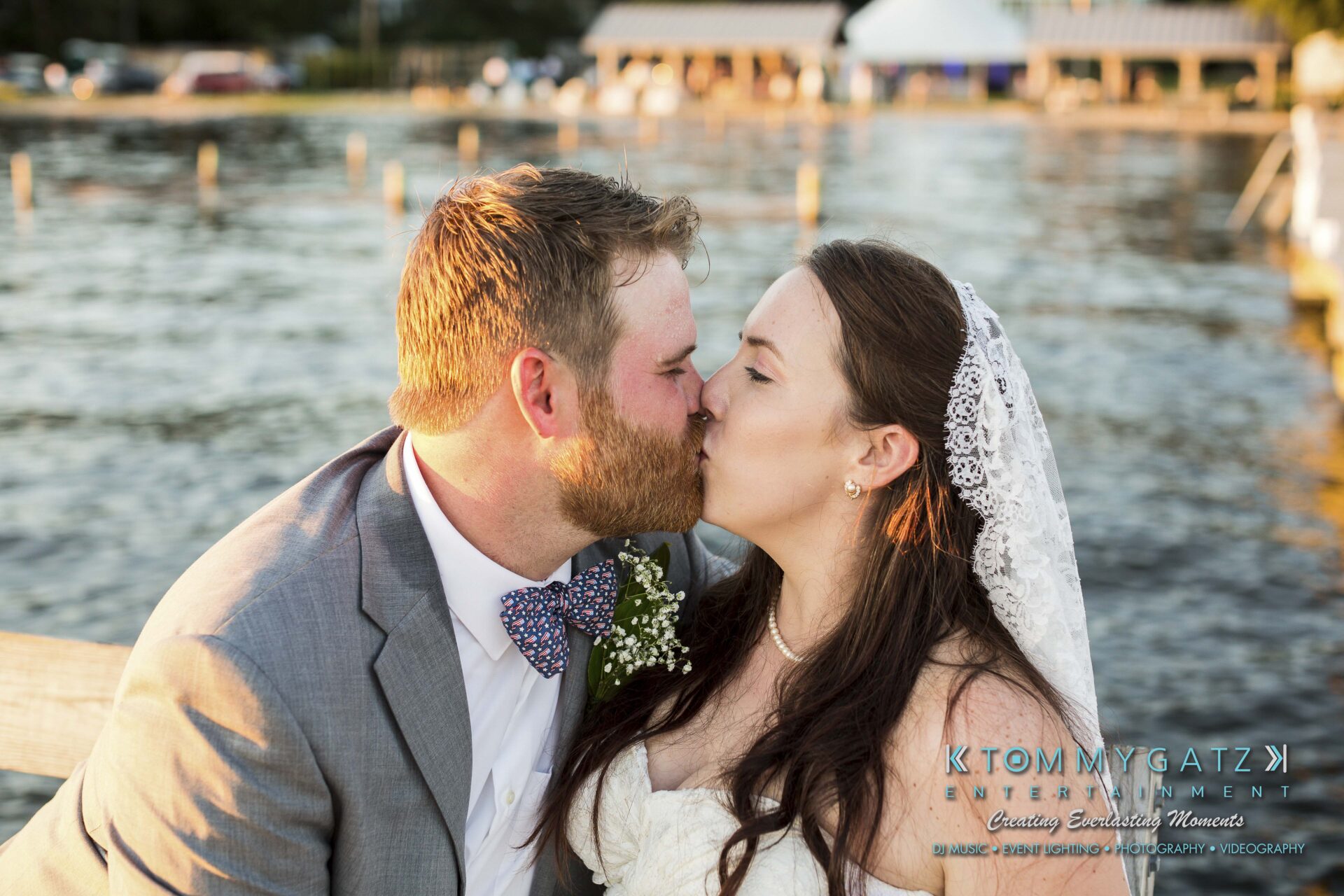 Ann-Marie-Alex-92317-FORMALS-Low-Res-WM-40 - TOMMY GATZ ENTERTAINMENT Couple in wedding attire kissing by a lake, with the groom in a suit and the bride in a white dress and veil.