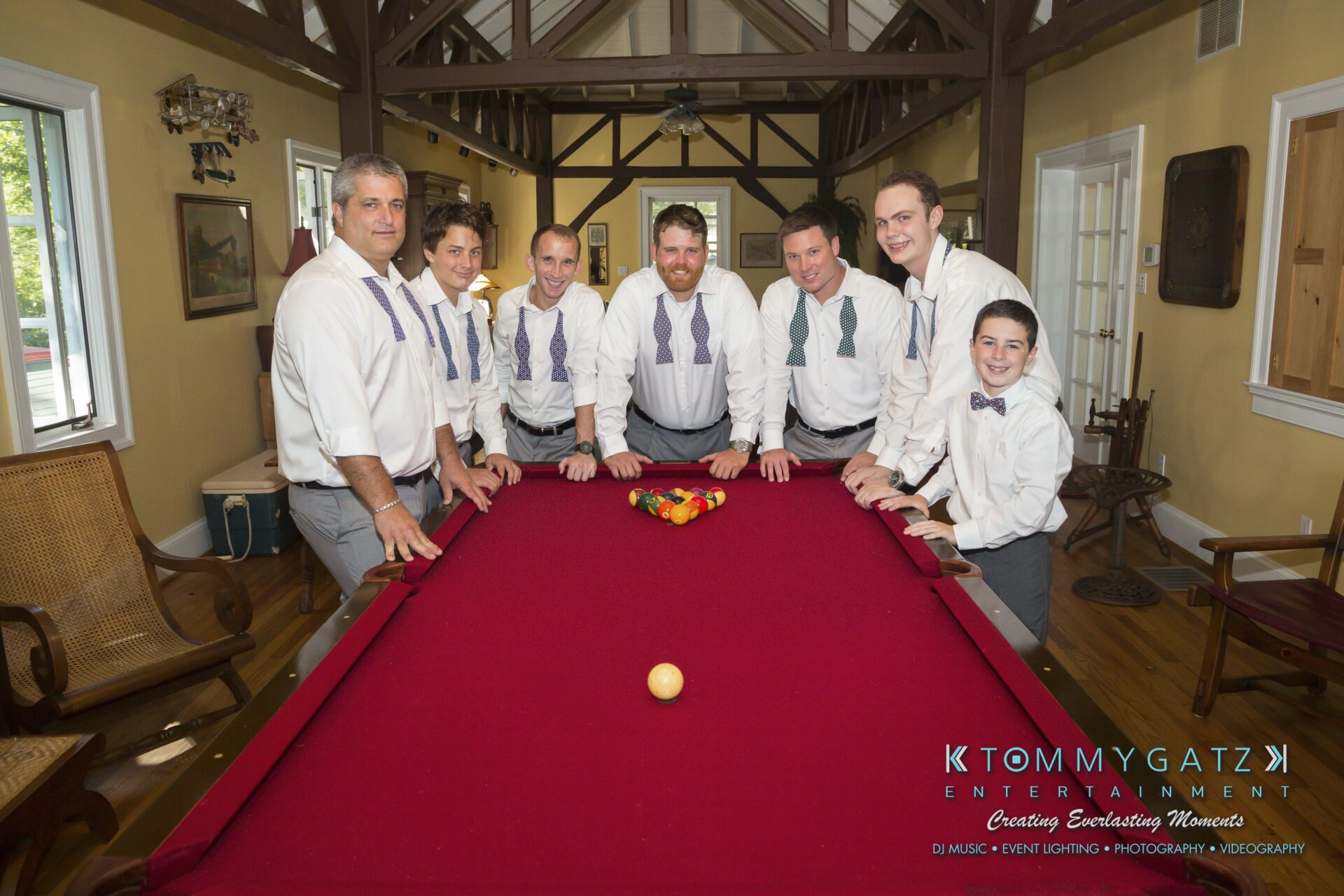 Ann-Marie-Alex-92317-PREP-Low-Res-WM-105 - TOMMY GATZ ENTERTAINMENT A group of seven men and a boy, all dressed in formal attire with bow ties, stand around a red pool table with a rack of billiard balls.