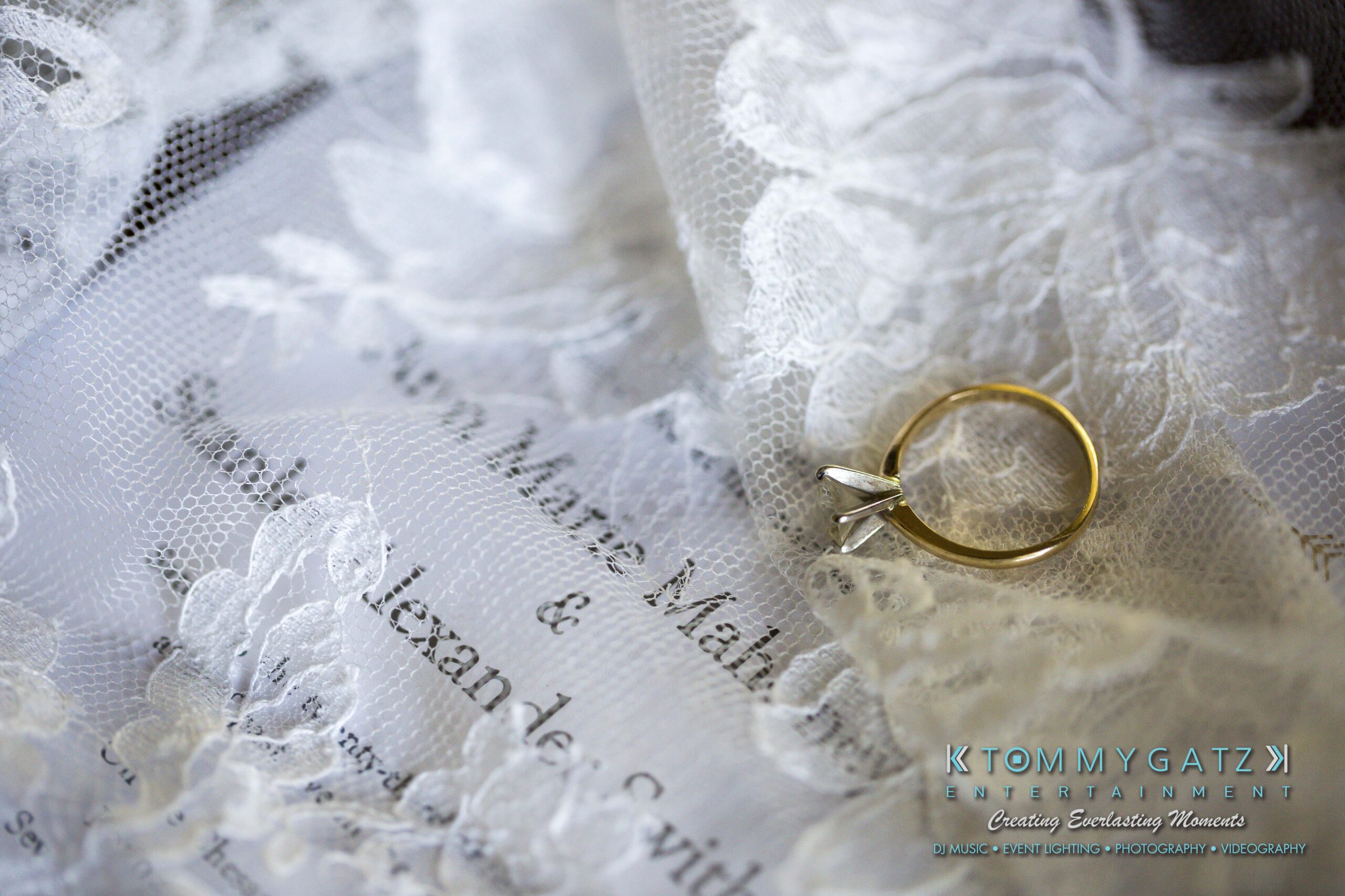 Ann-Marie-Alex-92317-PREP-Low-Res-WM-108 - TOMMY GATZ ENTERTAINMENT A gold ring with small diamond-shaped stones rests on lace fabric covering an invitation with the word "Mah" visible.