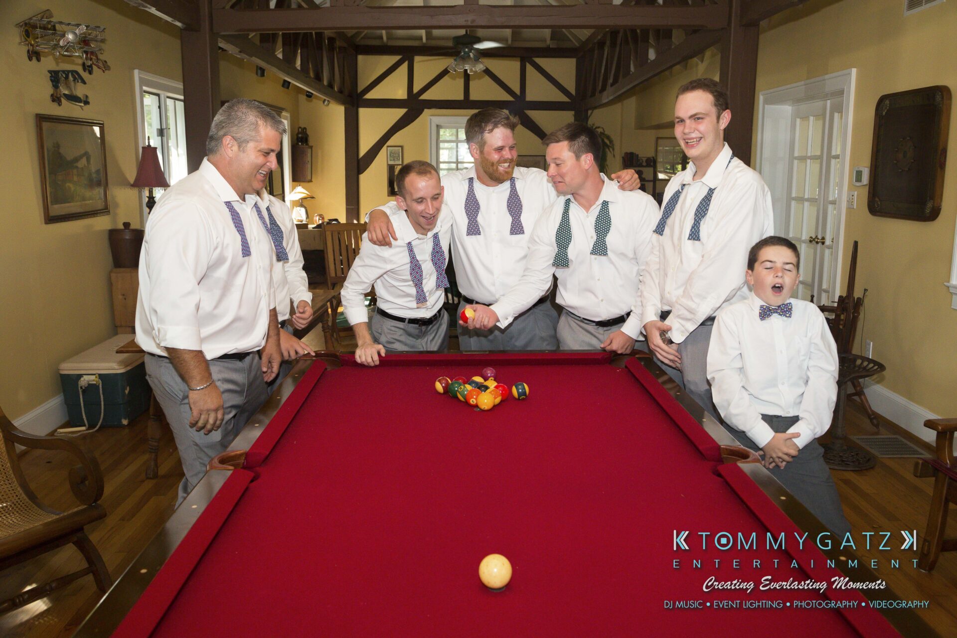 Ann-Marie-Alex-92317-PREP-Low-Res-WM-110 - TOMMY GATZ ENTERTAINMENT Six men in dress shirts and bow ties gather around a red pool table, smiling and chatting, with a young boy also present.
