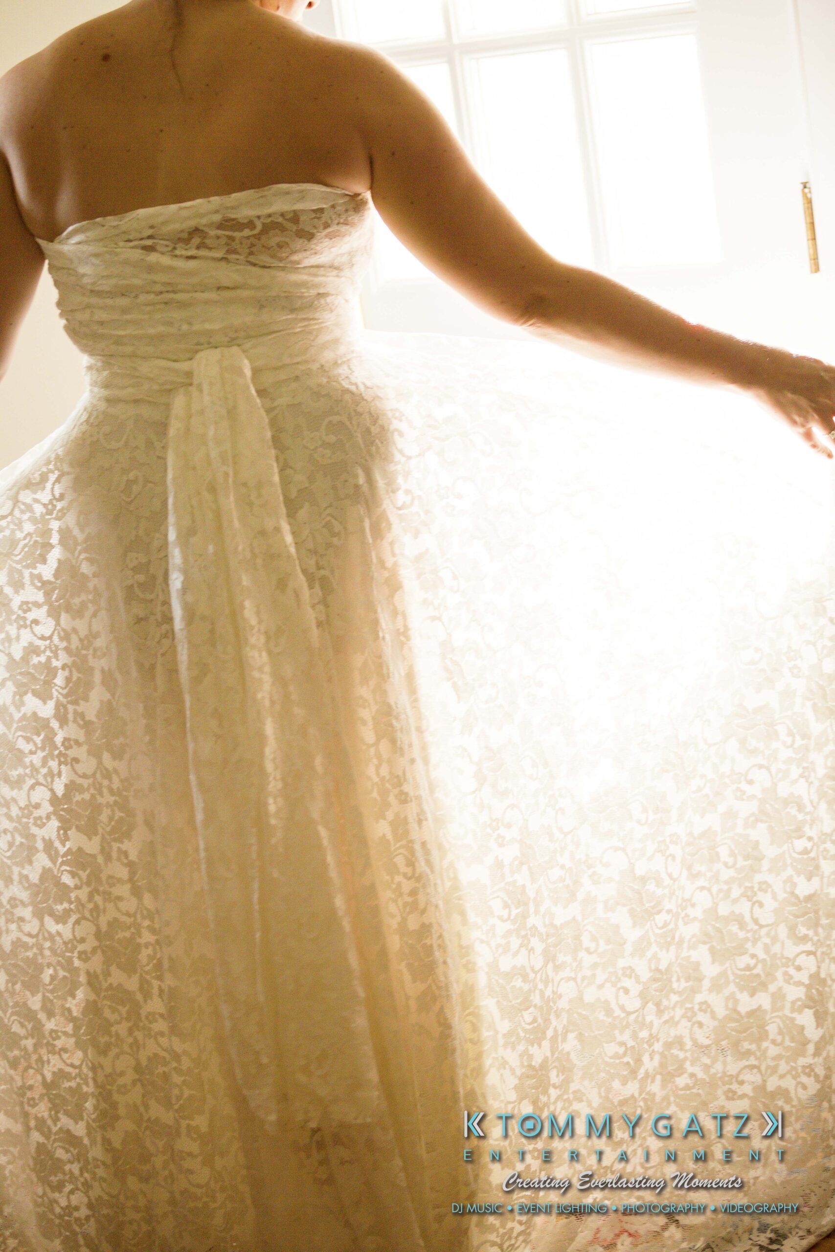 Ann-Marie-Alex-92317-PREP-Low-Res-WM-129 - TOMMY GATZ ENTERTAINMENT A person in a strapless white lace dress stands in front of a window, holding the dress outwards.