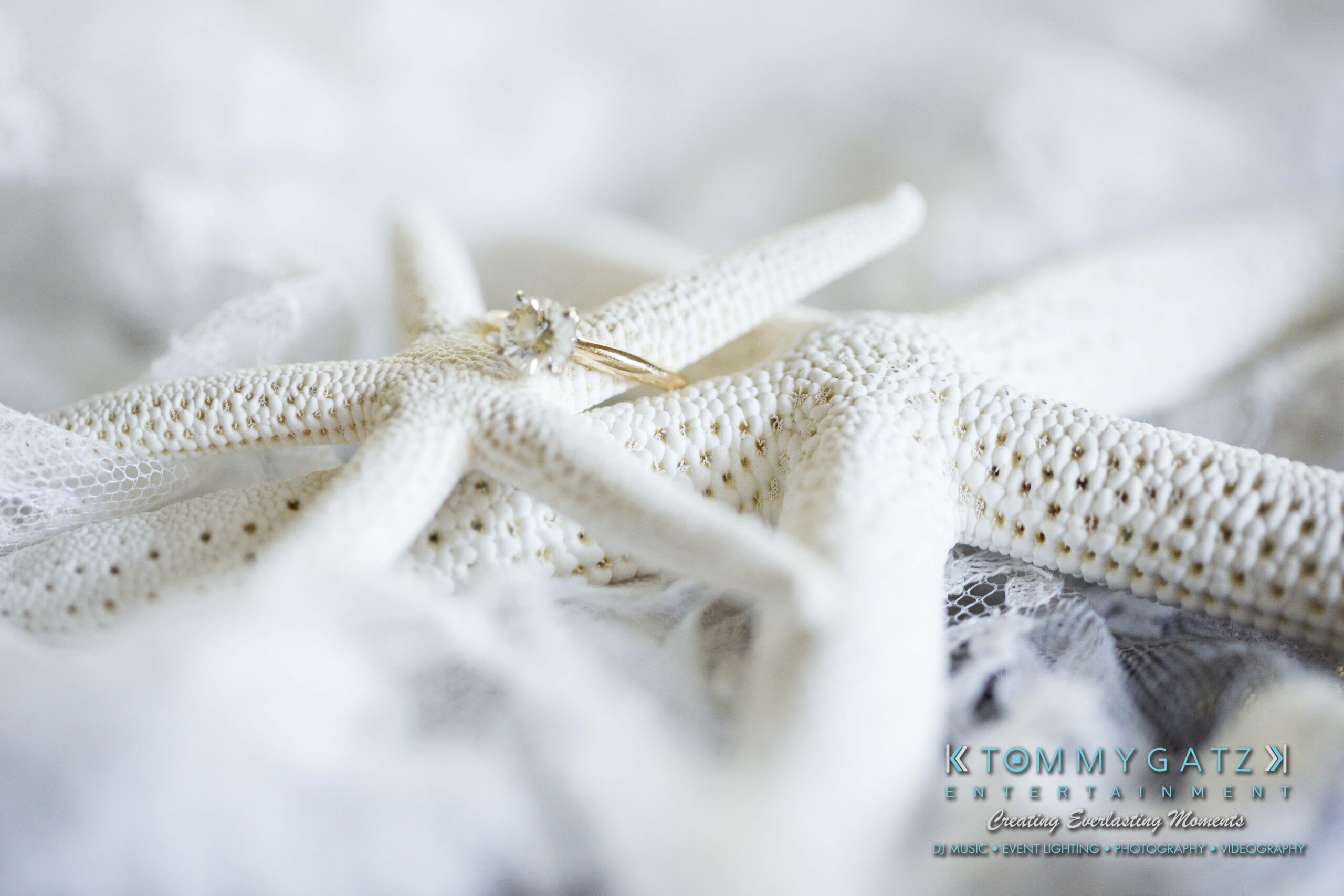 Ann-Marie-Alex-92317-PREP-Low-Res-WM-13 - TOMMY GATZ ENTERTAINMENT A diamond ring on a lace-covered starfish with text, "Tommy Gatz Entertainment," in the corner.