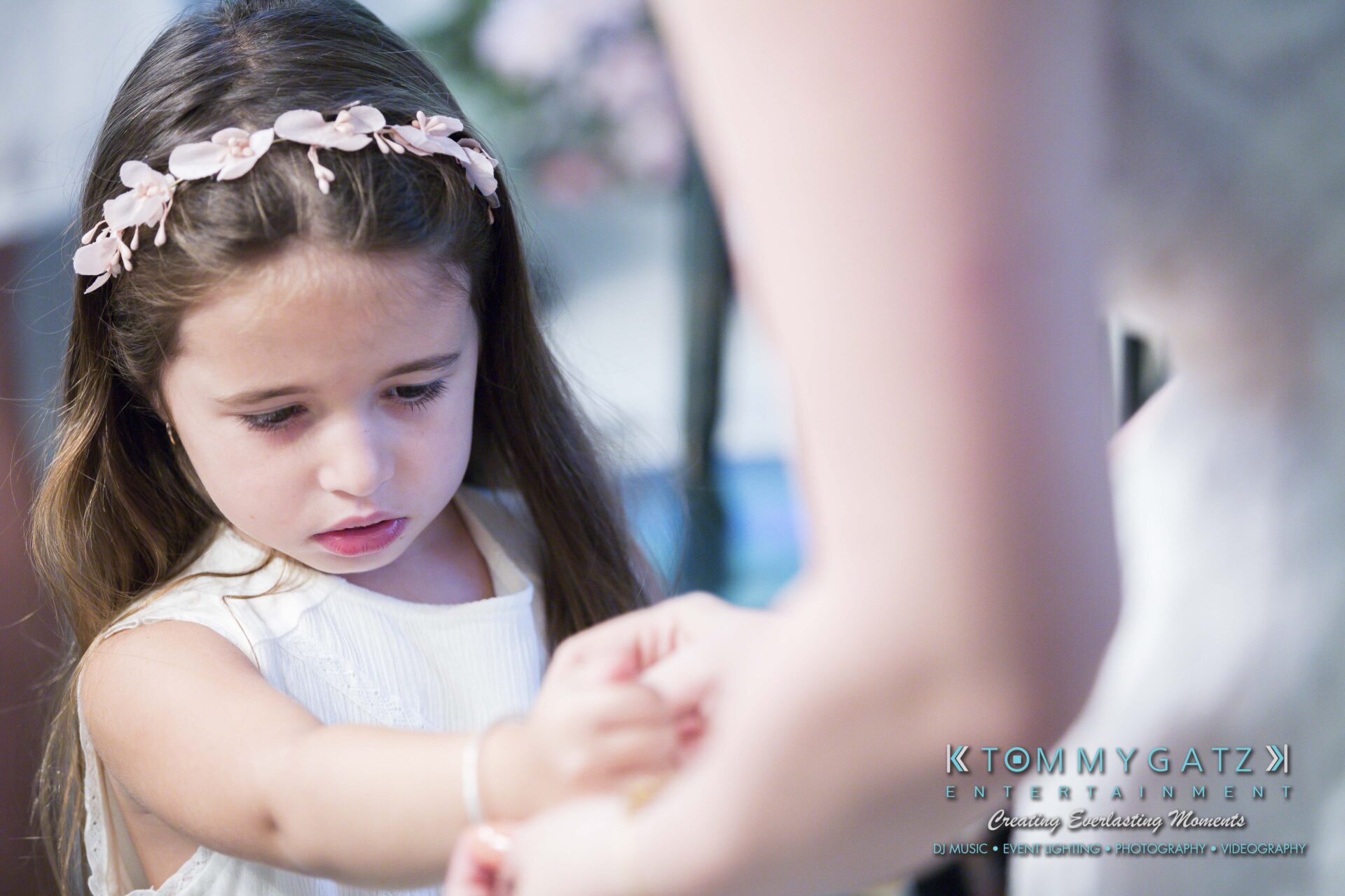 Ann-Marie-Alex-92317-PREP-Low-Res-WM-139 - TOMMY GATZ ENTERTAINMENT A young girl wearing a flower headband looks down, while holding an adult's hand.