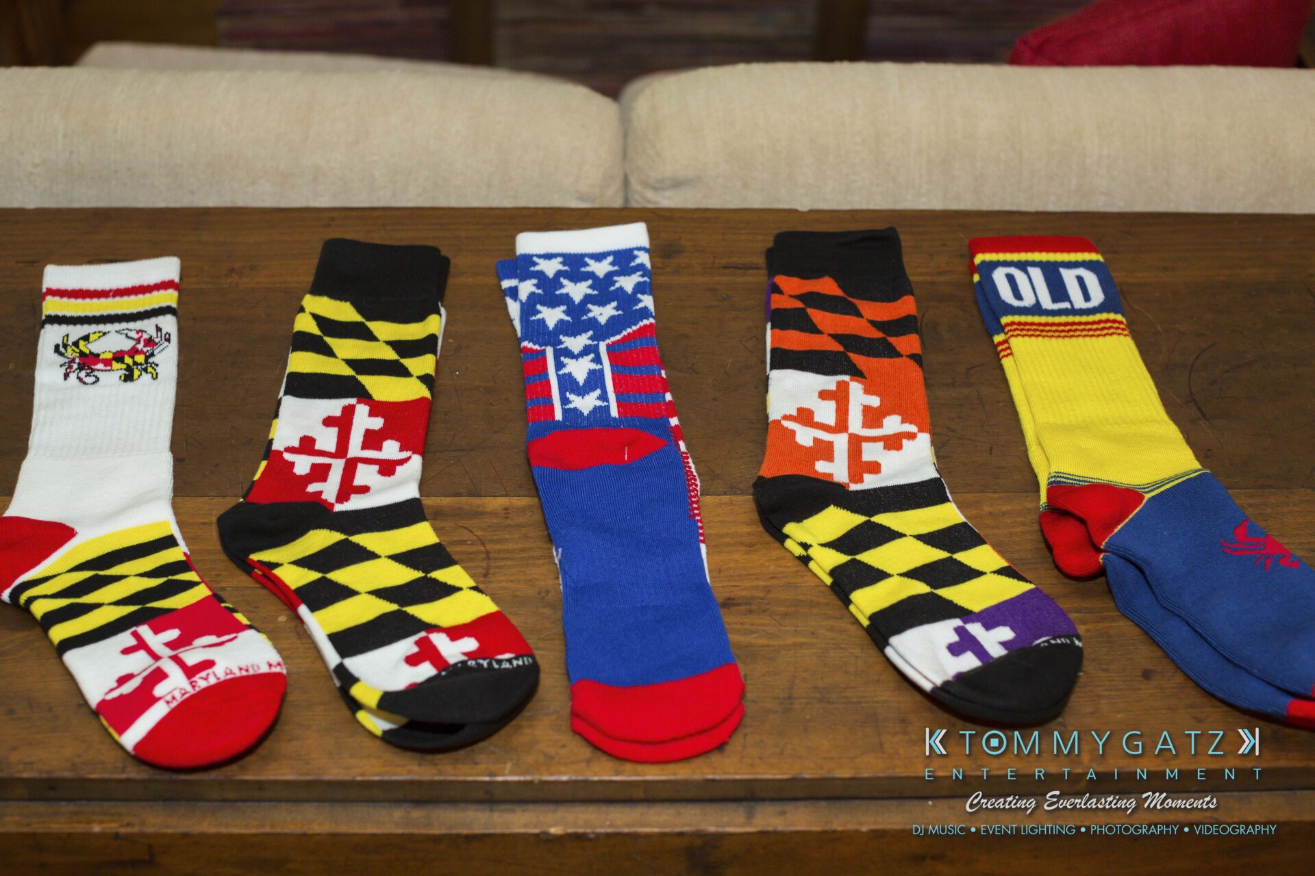 Ann-Marie-Alex-92317-PREP-Low-Res-WM-2 - TOMMY GATZ ENTERTAINMENT Five colorful Maryland-themed socks with various designs are displayed on a wooden surface.