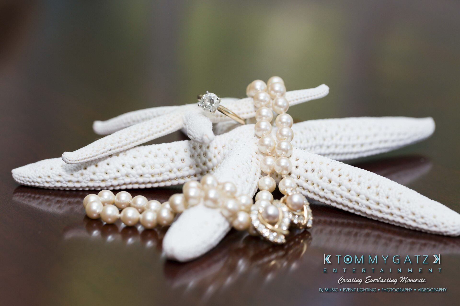 Ann-Marie-Alex-92317-PREP-Low-Res-WM-60 - TOMMY GATZ ENTERTAINMENT Pearl jewelry and a diamond ring displayed on a decorative white starfish, with a Tommy Gatz Entertainment logo in the corner.