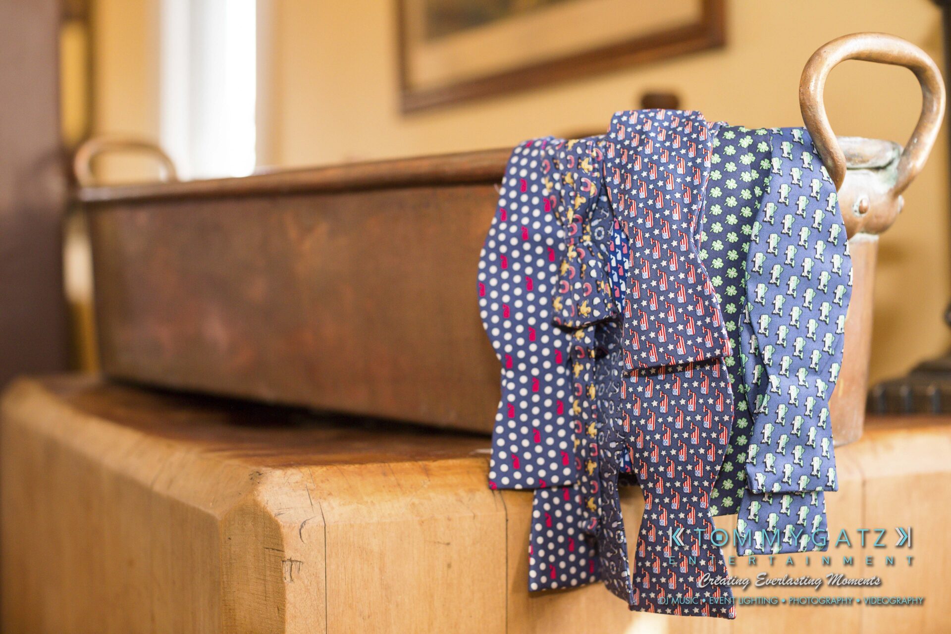 Ann-Marie-Alex-92317-PREP-Low-Res-WM-68 - TOMMY GATZ ENTERTAINMENT A collection of colorful neckties with various patterns draped over a large copper pot on a wooden surface.