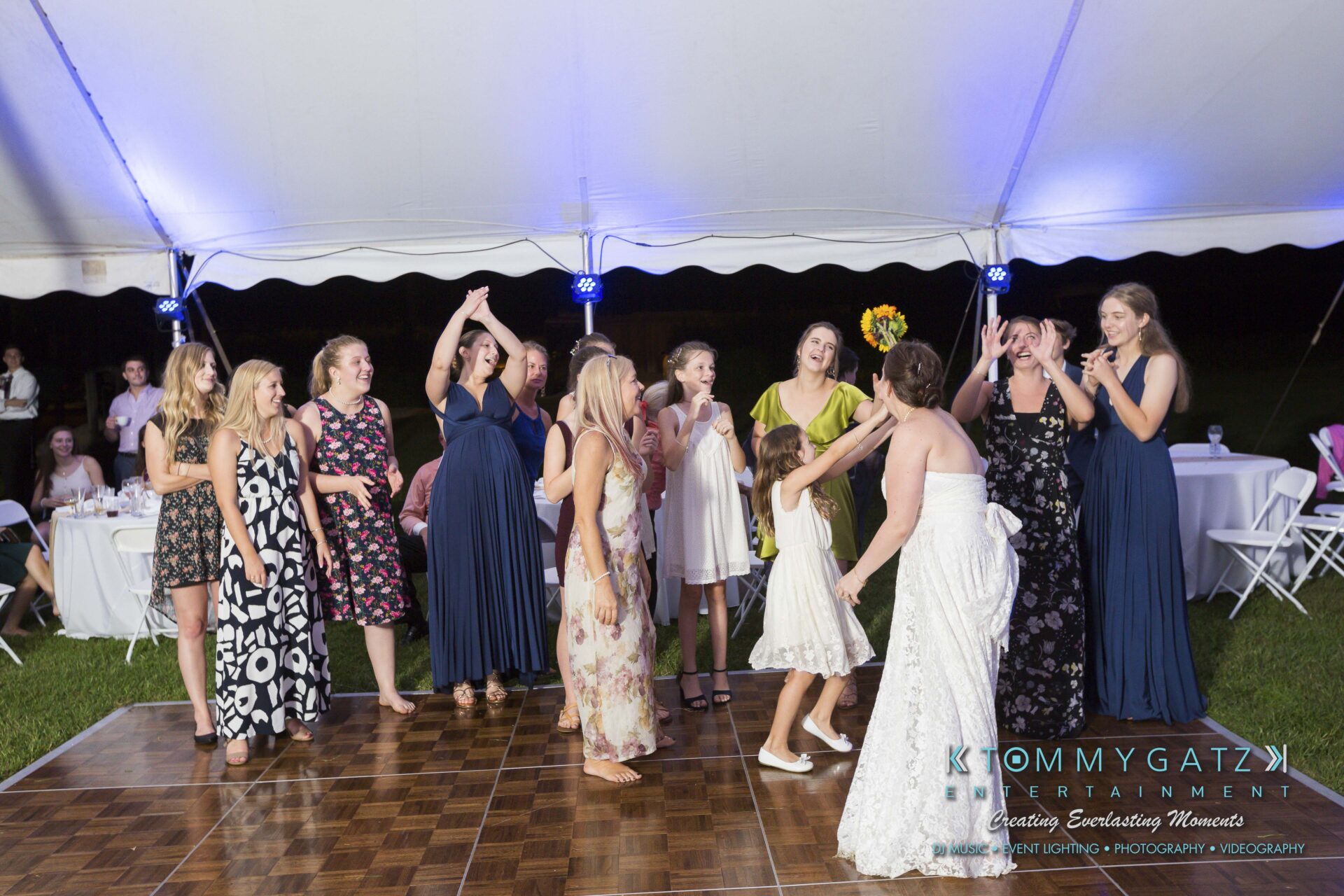 Ann-Marie-Alex-92317-RECEPTION-Low-Res-WM-113 - TOMMY GATZ ENTERTAINMENT A bride tosses her bouquet to a group of women under a white tent at a wedding reception.