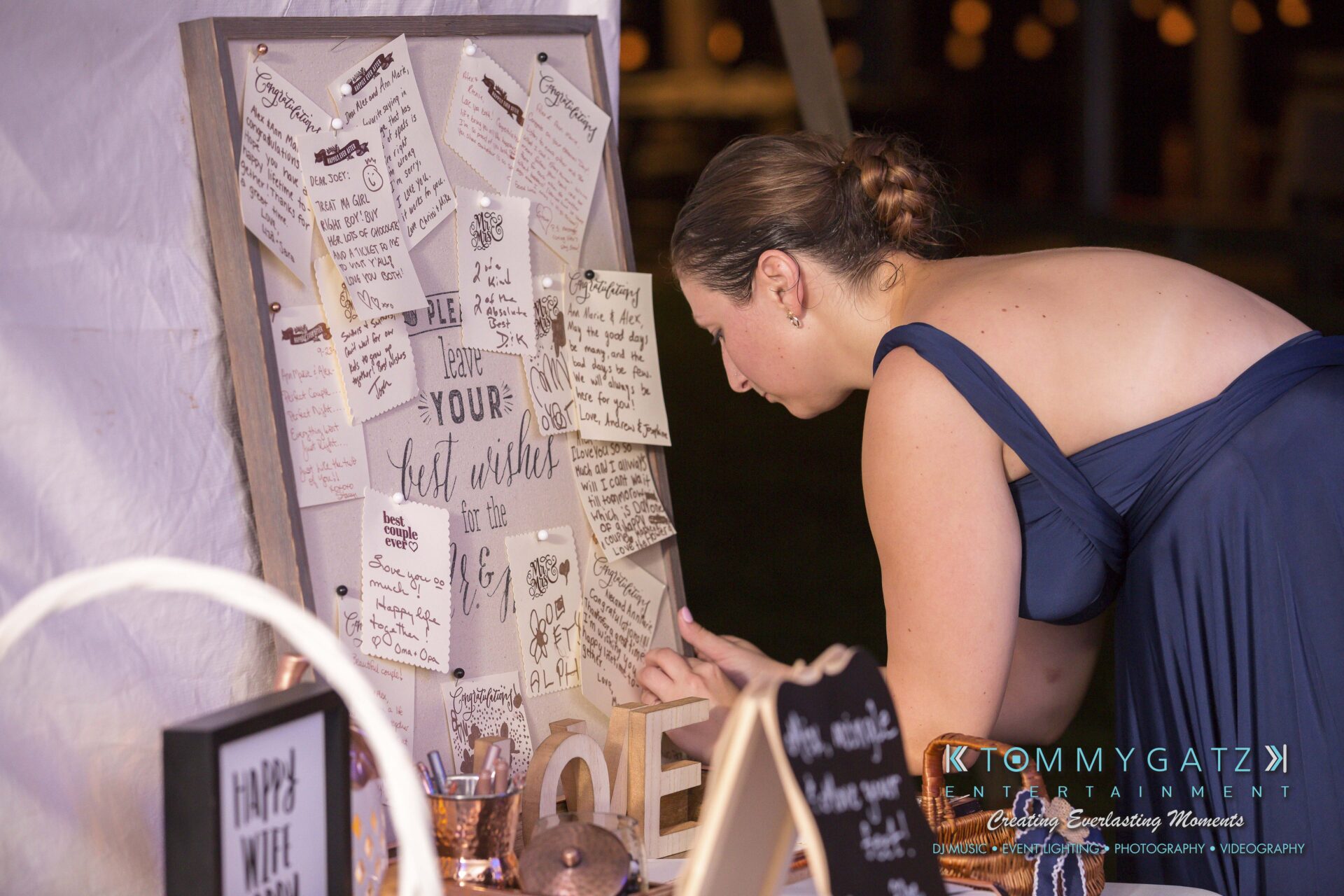 Ann-Marie-Alex-92317-RECEPTION-Low-Res-WM-127 - TOMMY GATZ ENTERTAINMENT A woman in a blue dress writes on a note at a wooden board displaying various handwritten messages.
