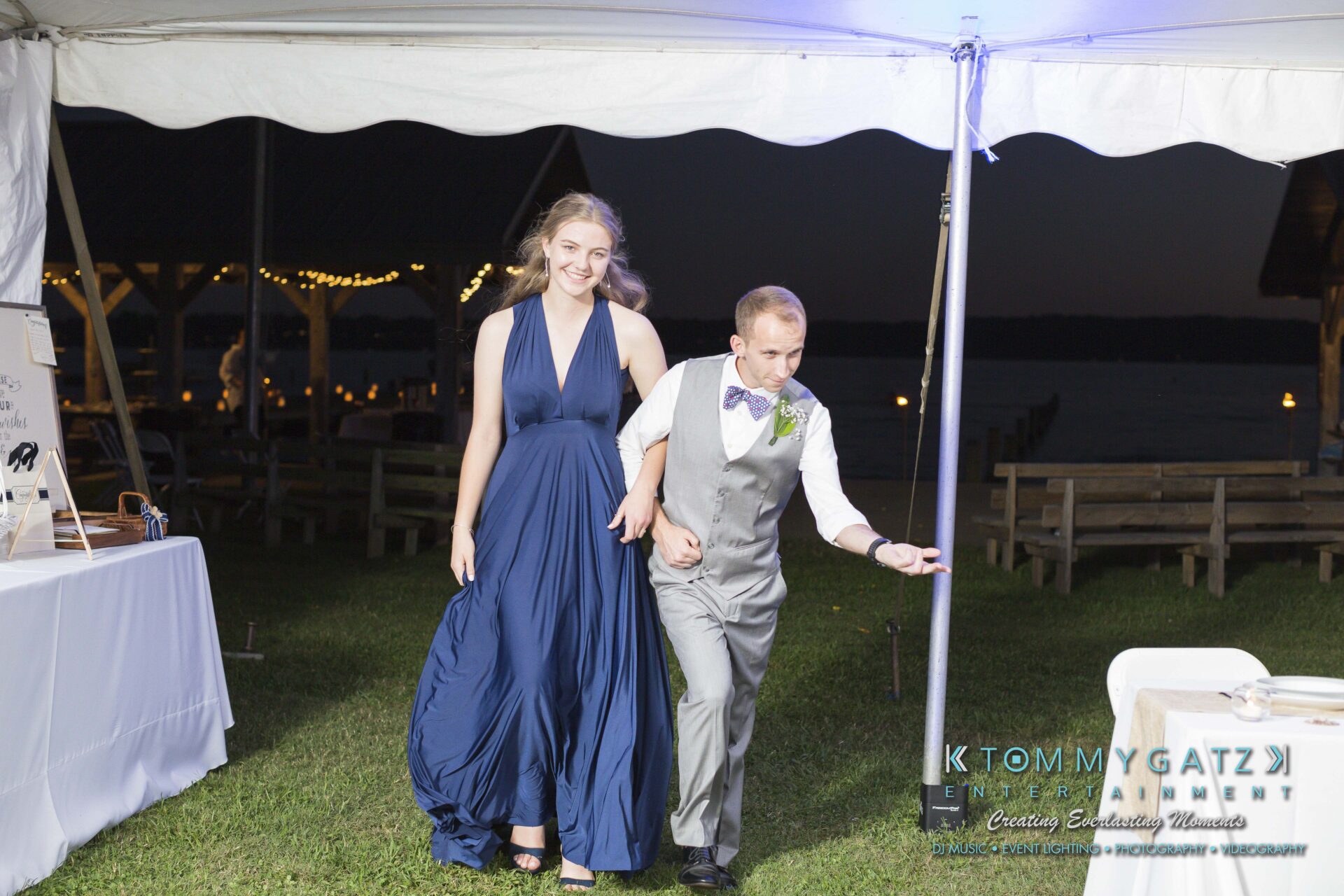 Ann-Marie-Alex-92317-RECEPTION-Low-Res-WM-19 - TOMMY GATZ ENTERTAINMENT A woman in a blue dress and a man in a gray suit enter a tented area at an outdoor event at night.