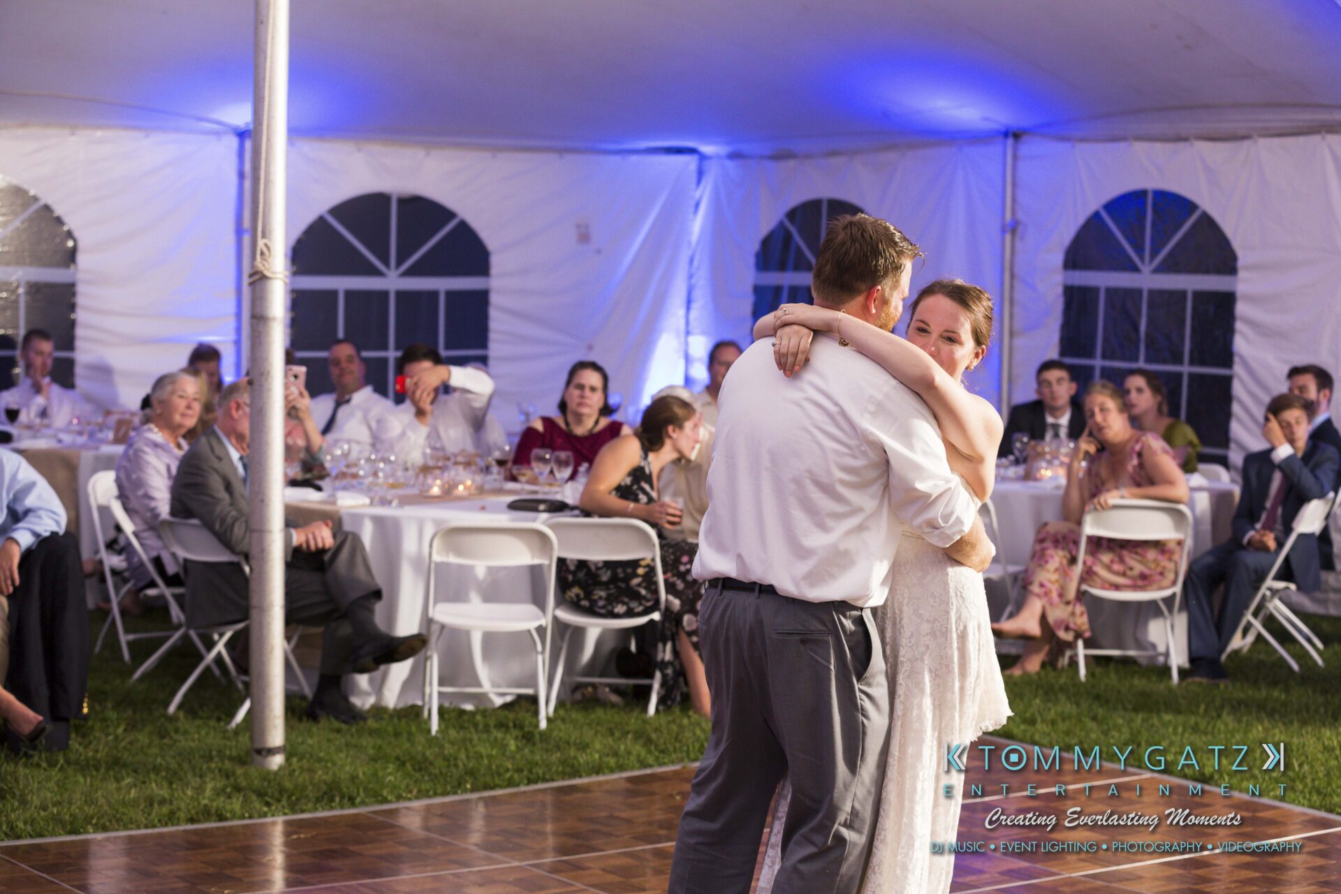 Ann-Marie-Alex-92317-RECEPTION-Low-Res-WM-62 - TOMMY GATZ ENTERTAINMENT A couple dances in a tented wedding reception surrounded by seated guests.