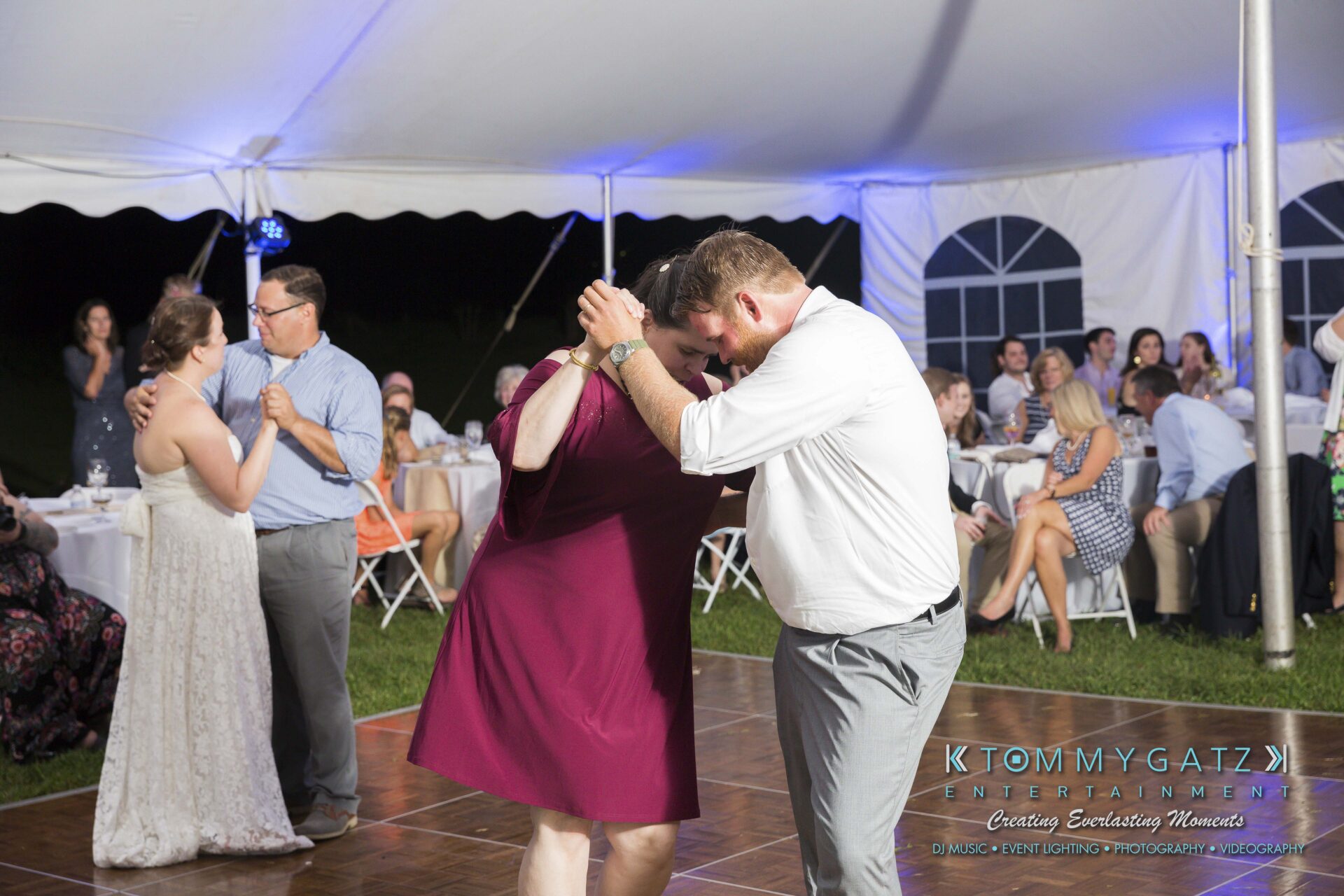 Ann-Marie-Alex-92317-RECEPTION-Low-Res-WM-68 - TOMMY GATZ ENTERTAINMENT A couple dances closely under a white tent, with other guests seated or dancing in the background.