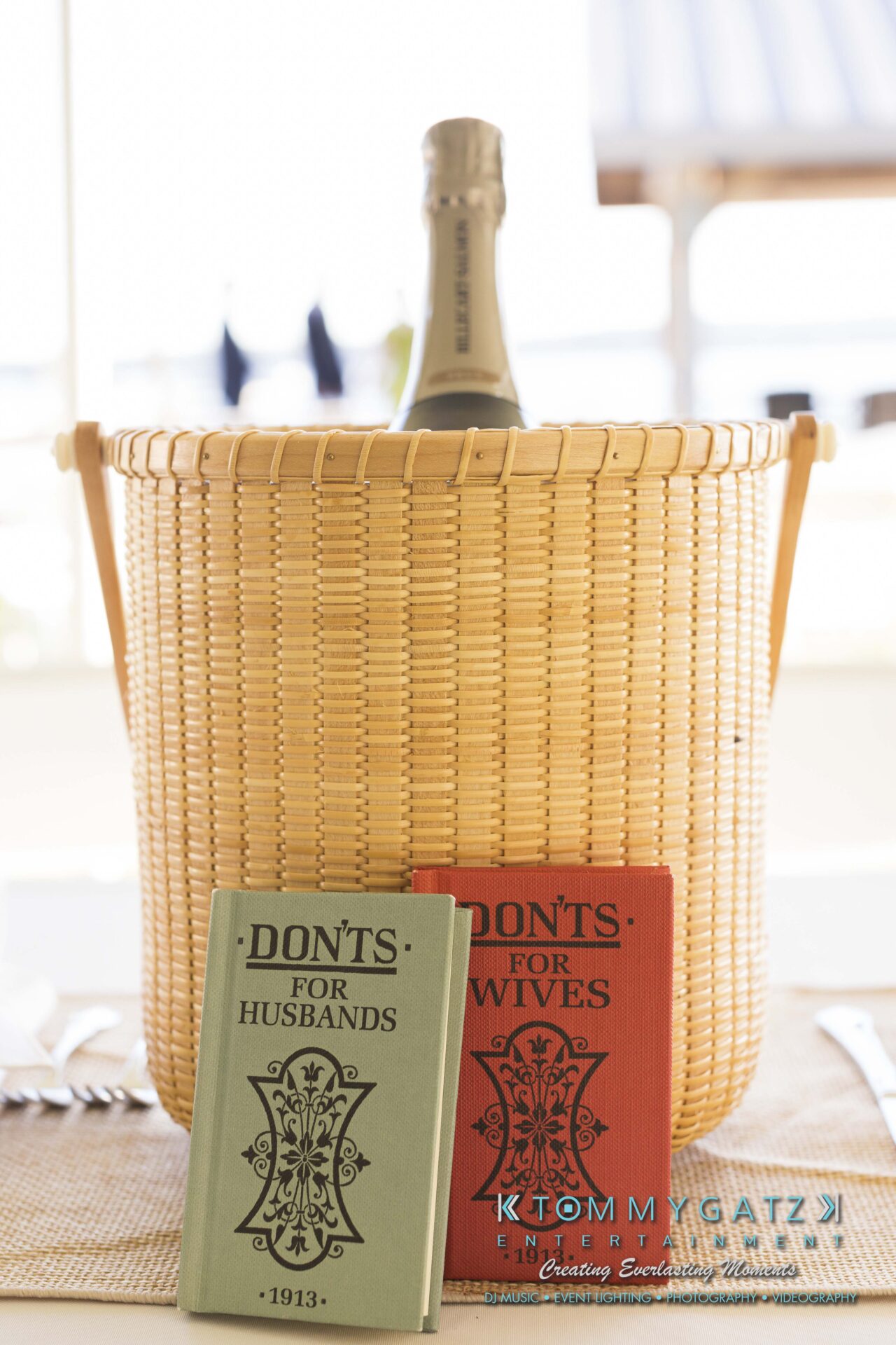 Ann-Marie-Alex-92317-RECEPTION-Low-Res-WM-8 - TOMMY GATZ ENTERTAINMENT A wicker basket holds a bottle of champagne. Two books titled "Don'ts for Husbands" and "Don'ts for Wives" are displayed in front.