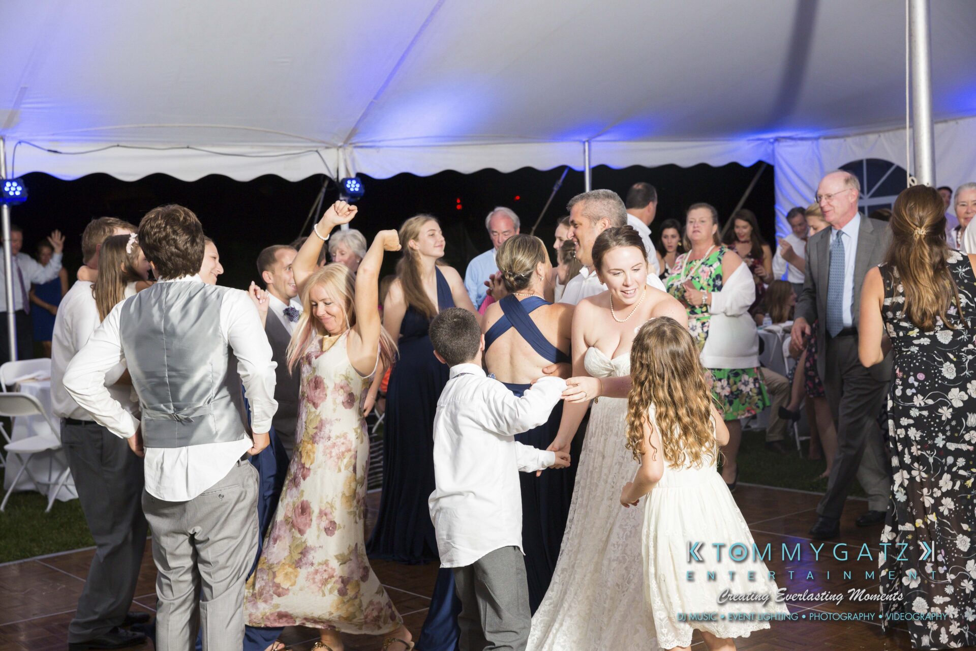 Ann-Marie-Alex-92317-RECEPTION-Low-Res-WM-82 - TOMMY GATZ ENTERTAINMENT A group of people dancing energetically under a large white tent at a nighttime event with a crowd watching.