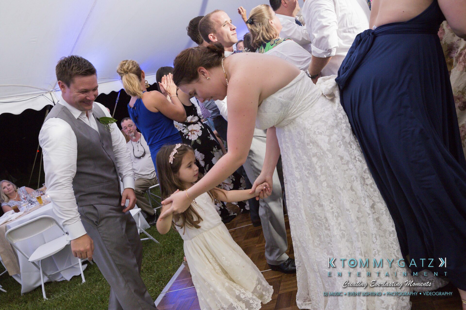 Ann-Marie-Alex-92317-RECEPTION-Low-Res-WM-88 - TOMMY GATZ ENTERTAINMENT A bride in a white dress dances with a young girl at a wedding reception, with guests in the background under a tent.