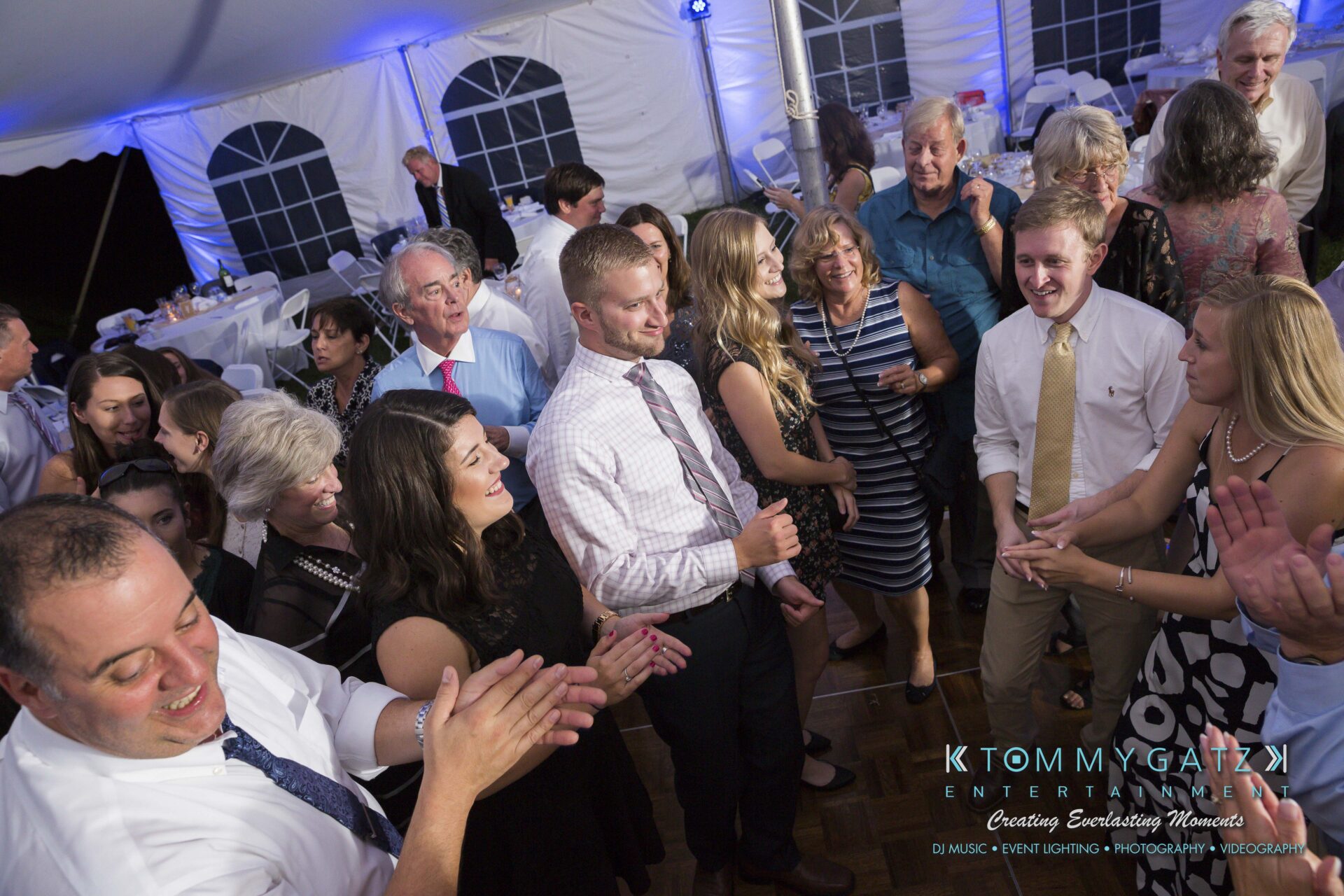 Ann-Marie-Alex-92317-RECEPTION-Low-Res-WM-89 - TOMMY GATZ ENTERTAINMENT A group of people are dancing and smiling in a tented event space.