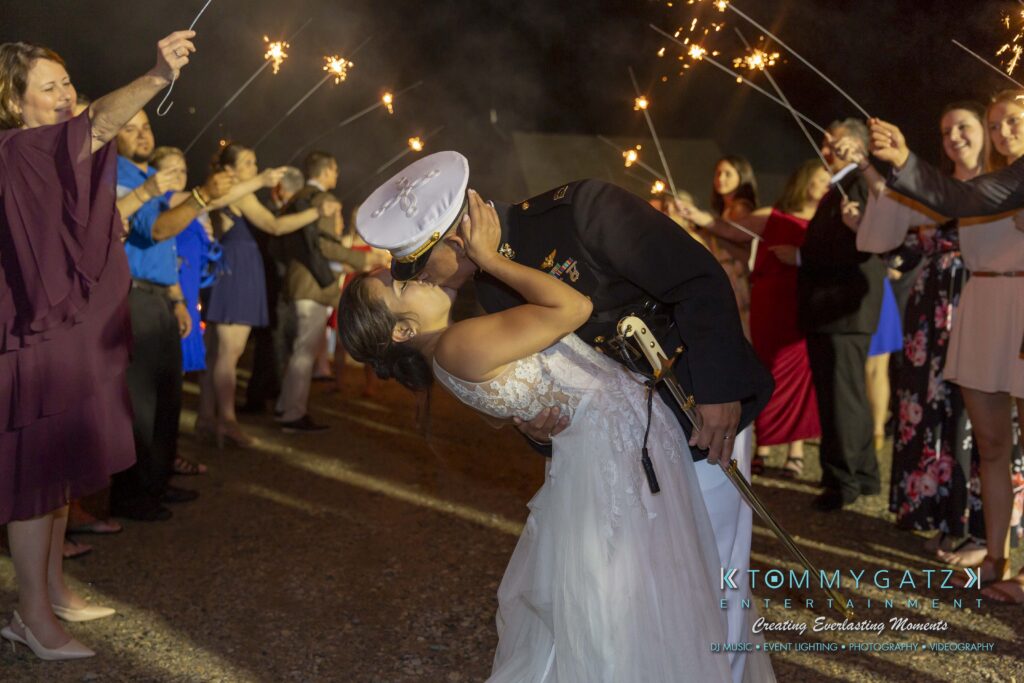 Annie-Casey-060918-RECEPTION-Low-Res-WM-1083 - TOMMY GATZ ENTERTAINMENT A bride and groom kiss surrounded by people holding sparklers at night. The groom is in military uniform, and the bride wears a white dress.