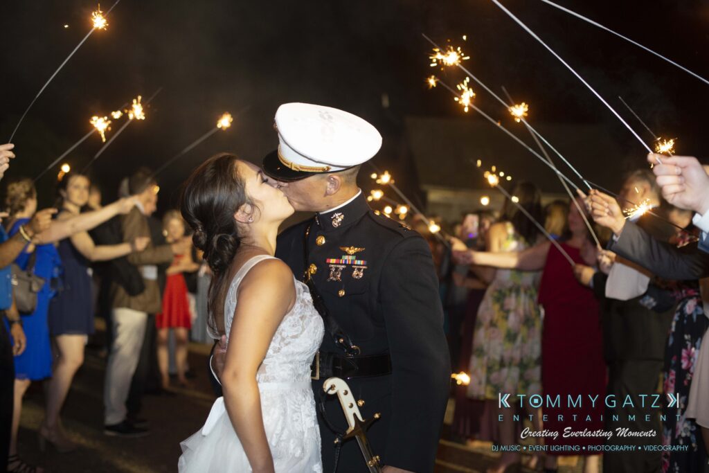 Annie-Casey-060918-RECEPTION-Low-Res-WM-1085 - TOMMY GATZ ENTERTAINMENT Bride and groom kiss under a sparklers tunnel, with guests holding sparklers and cheering in the background. The groom wears a military uniform.