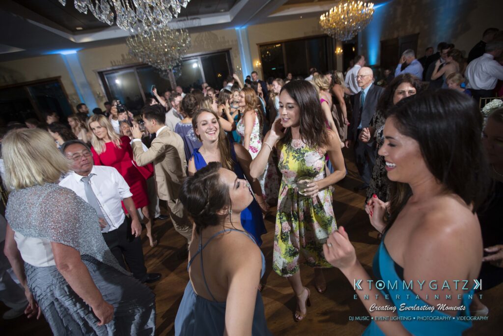 Annie-Casey-060918-RECEPTION-Low-Res-WM-974 - TOMMY GATZ ENTERTAINMENT A lively wedding reception with guests dancing under a chandelier, featuring people in formal attire enjoying the event.