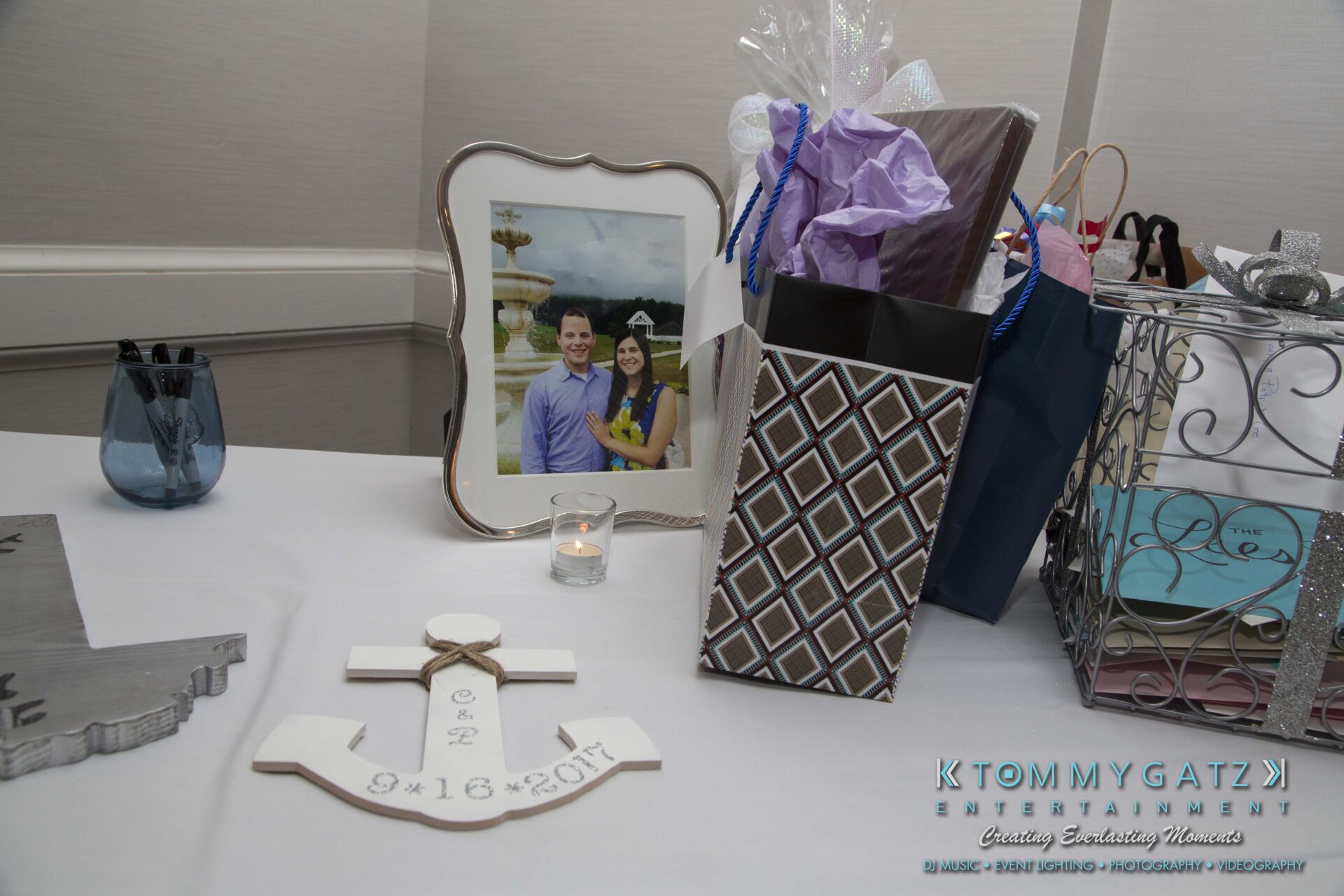 Carly-Patrick-FINAL-Blog-Watermark-10 - TOMMY GATZ ENTERTAINMENT A wedding gift table with wrapped presents, a framed photo of a couple, a candle, and a decorative anchor with the date 9-16-2017 on it.