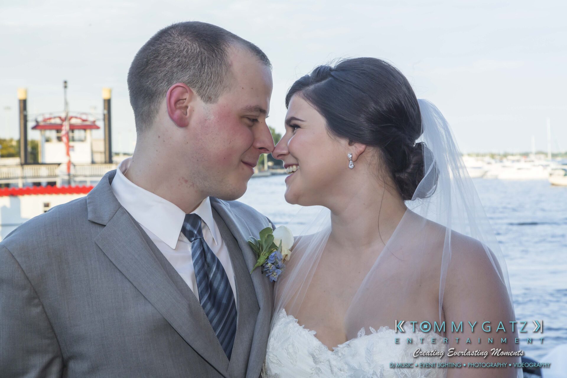 Carly-Patrick-FINAL-Blog-Watermark-19 - TOMMY GATZ ENTERTAINMENT A bride and groom smiling at each other in front of a marina backdrop.