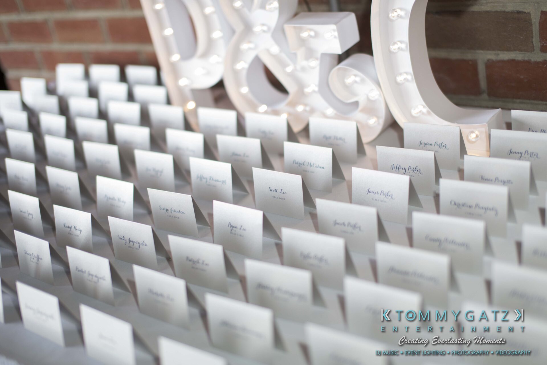 Carly-Patrick-FINAL-Blog-Watermark-3 - TOMMY GATZ ENTERTAINMENT Rows of wedding place cards on a table with illuminated letters in the background.