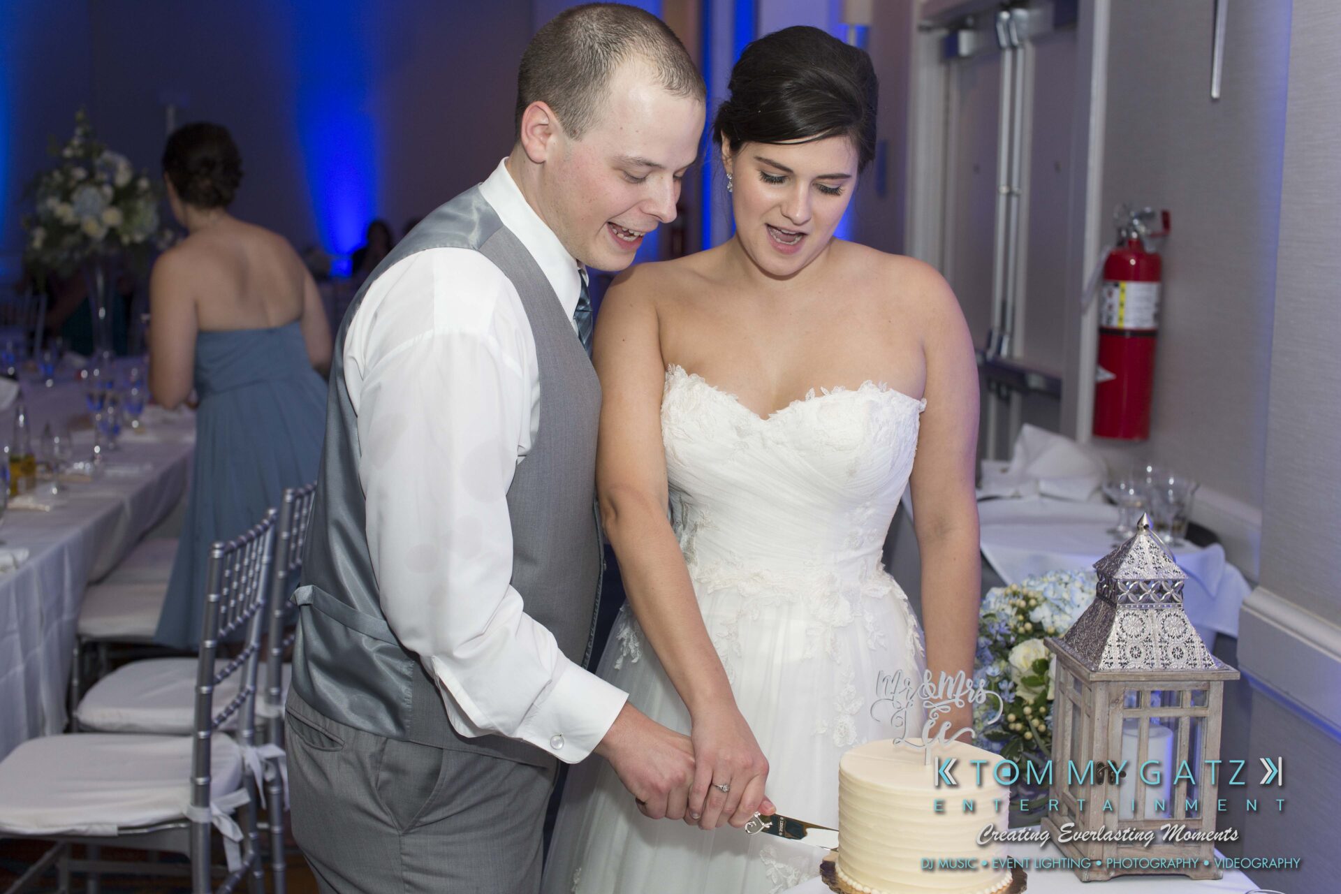 Carly-Patrick-FINAL-Blog-Watermark-41 - TOMMY GATZ ENTERTAINMENT A bride and groom are cutting a wedding cake together in a decorated reception area.